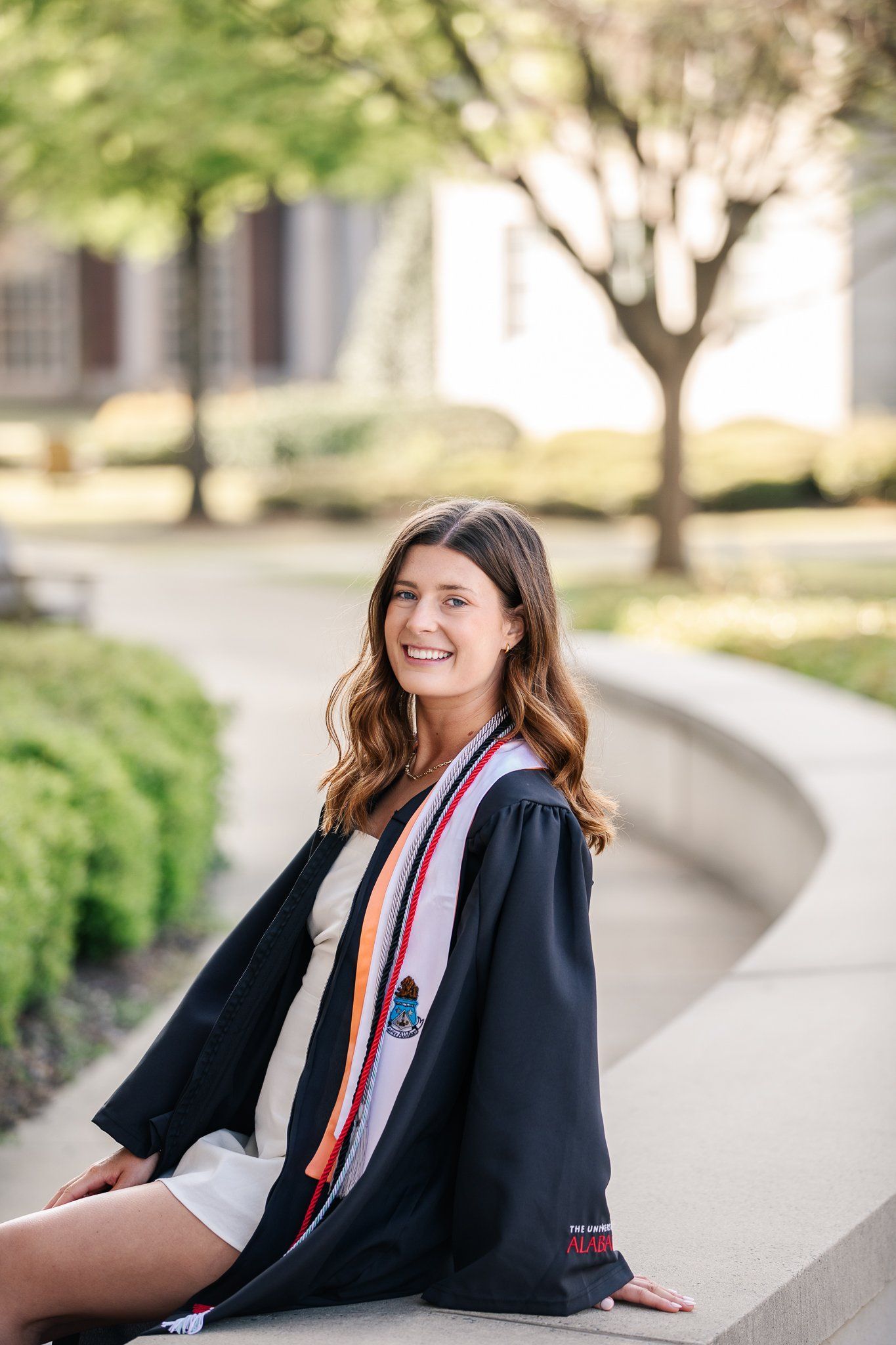 A woman in a graduation cap and gown is sitting on a bench.