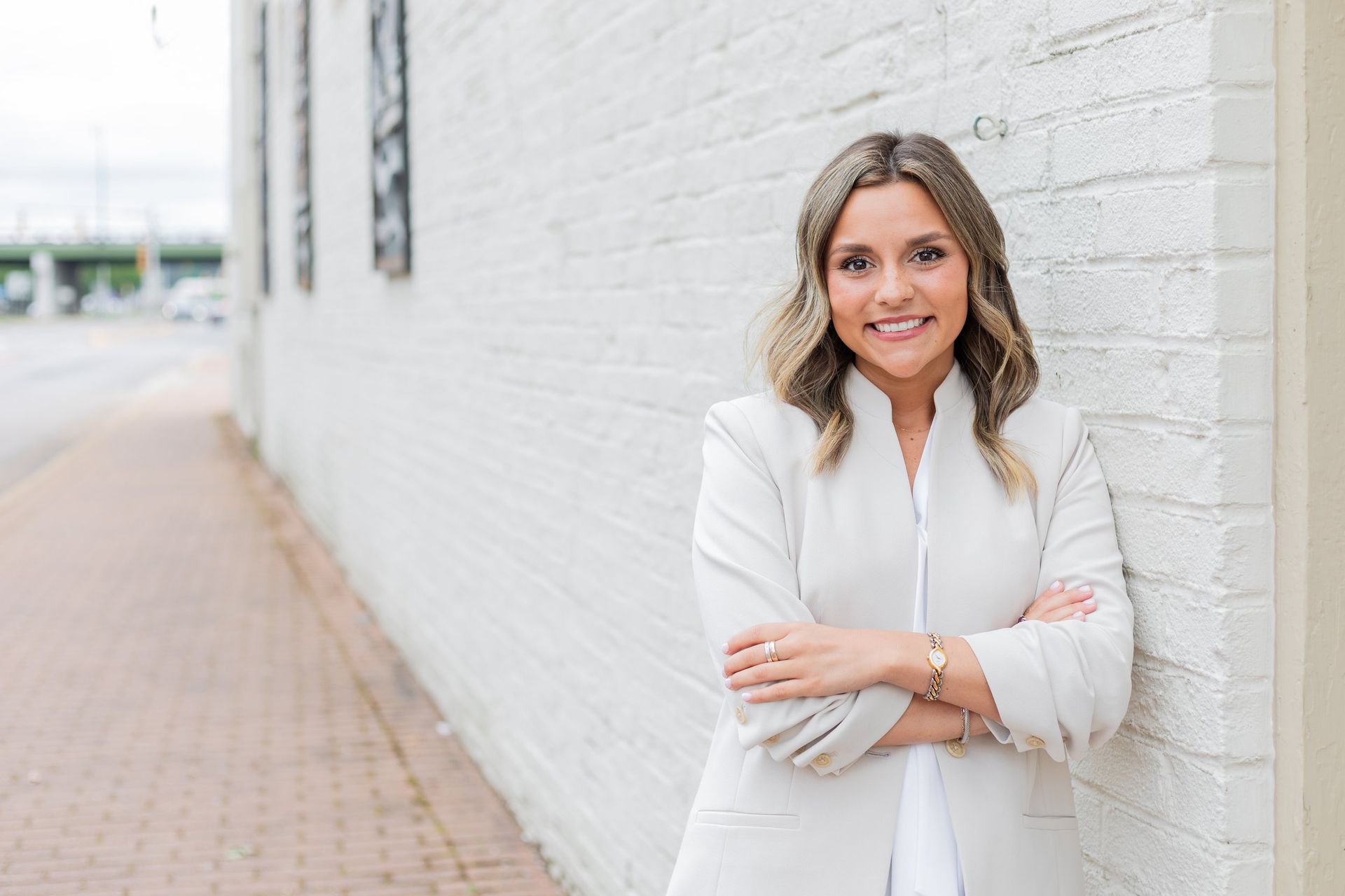 A woman is standing in front of a white brick wall with her arms crossed.