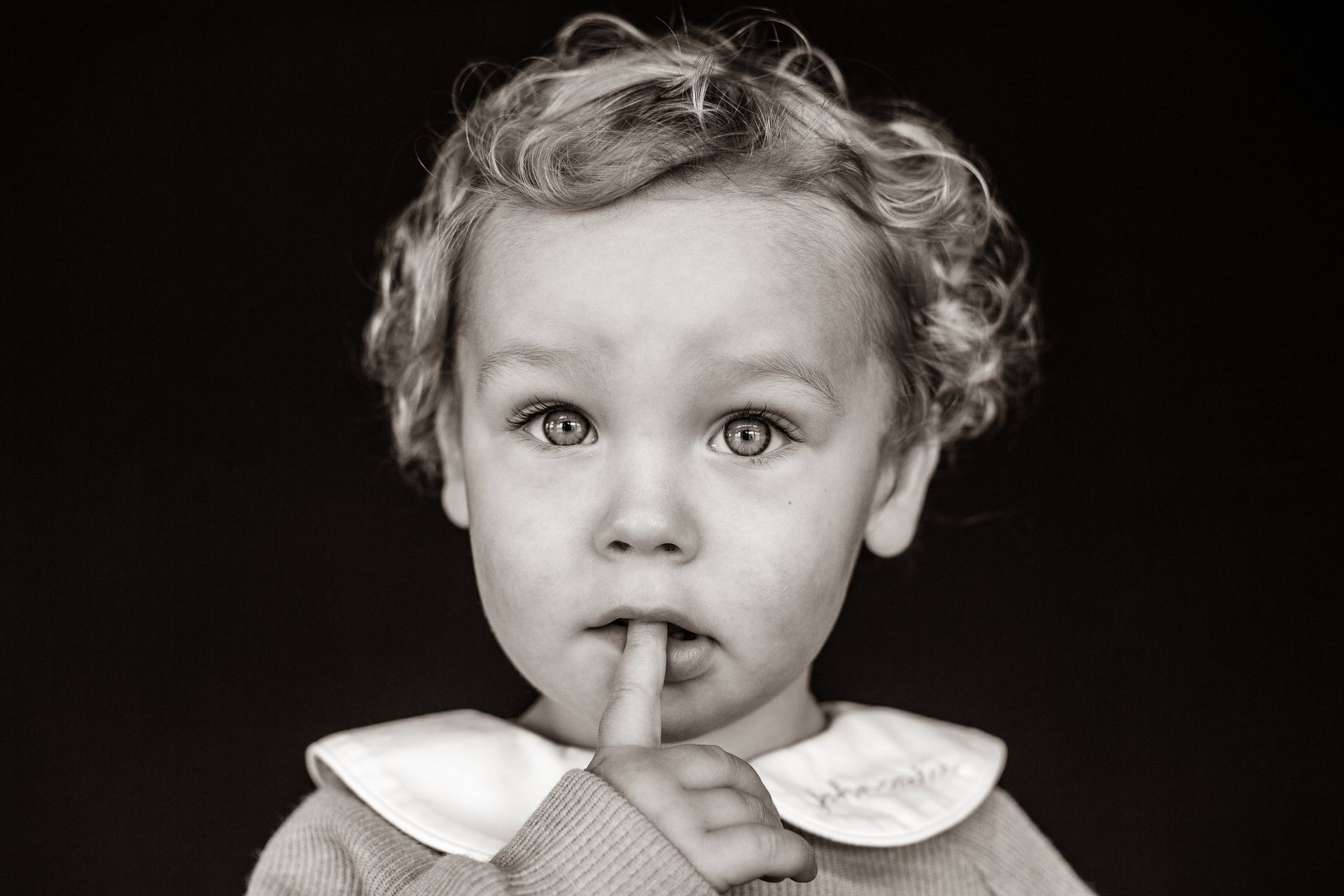 A little girl is holding her finger to her mouth.
