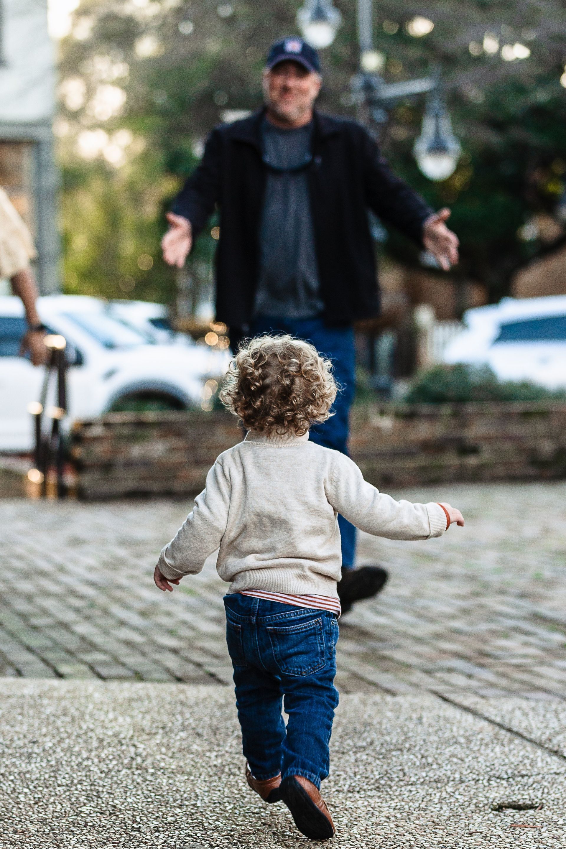 A little boy is running towards a man on a sidewalk.