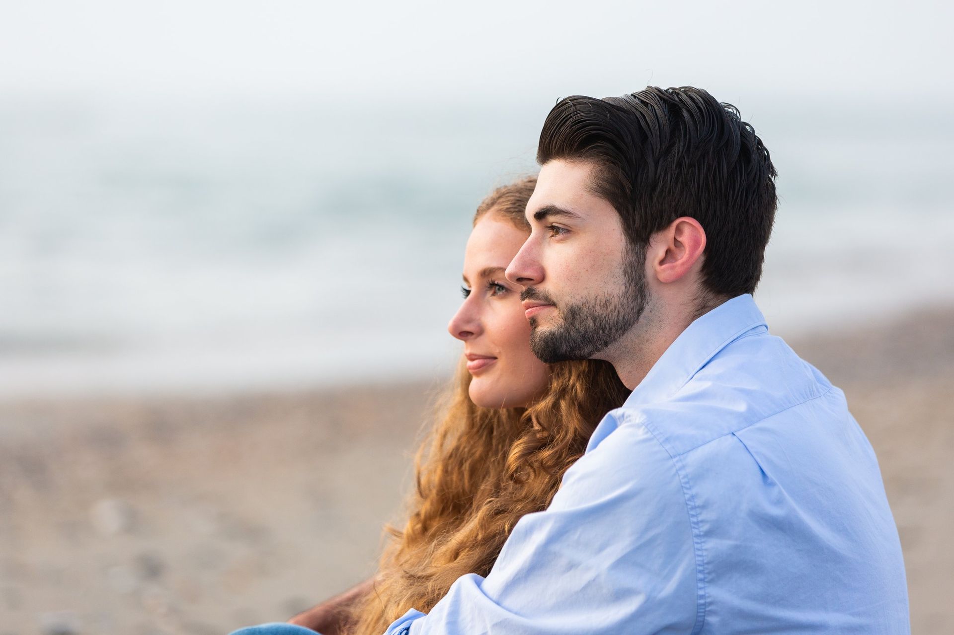 A man and a woman are sitting on the beach looking at the ocean.