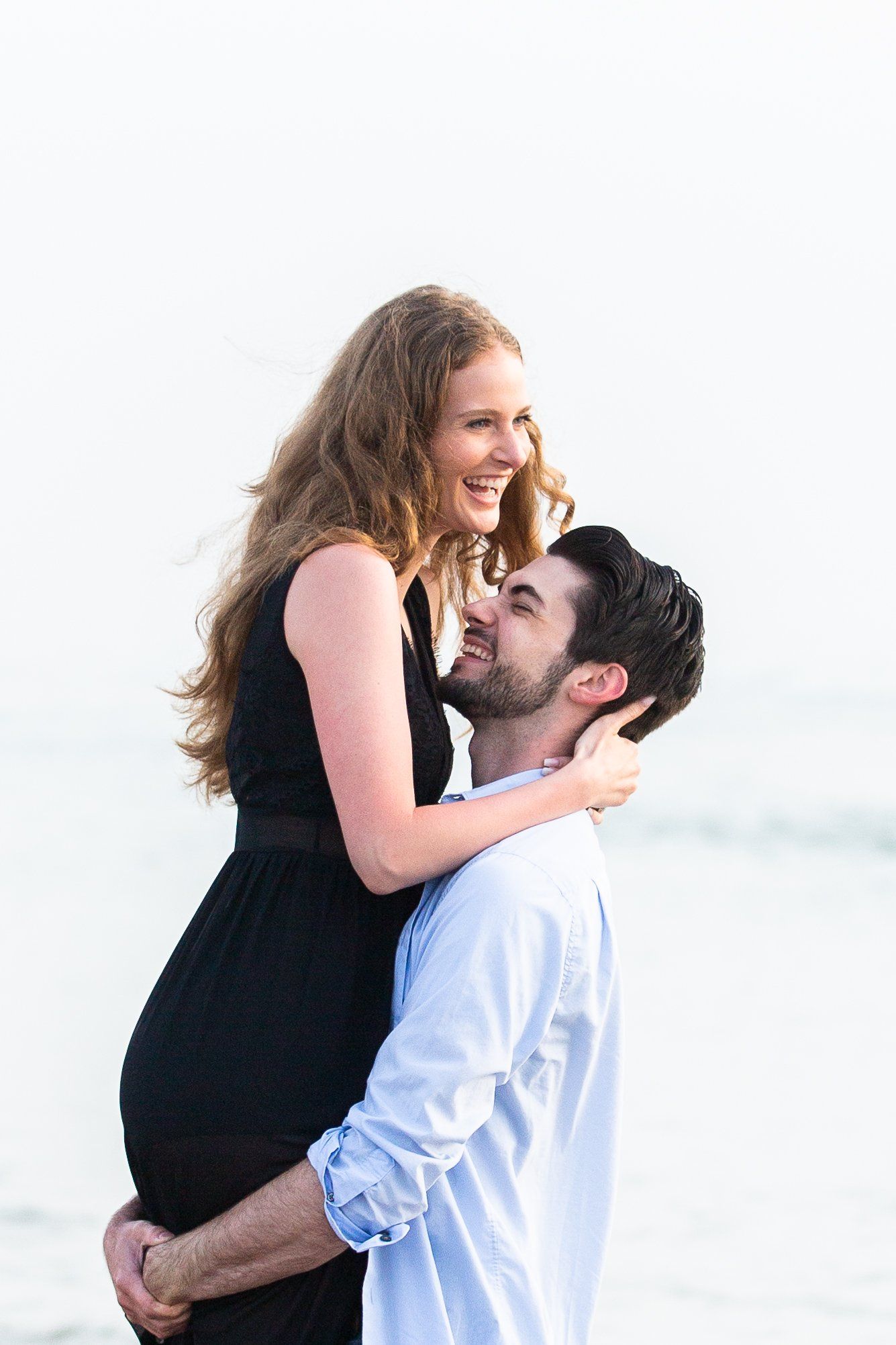 A man is holding a woman in his arms on the beach.