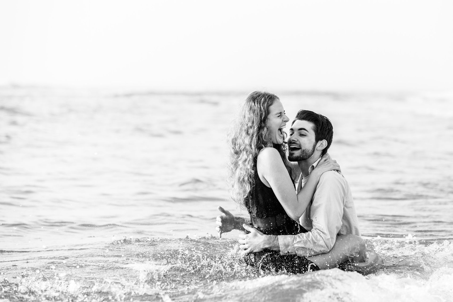 A black and white photo of a man and woman sitting in the ocean.