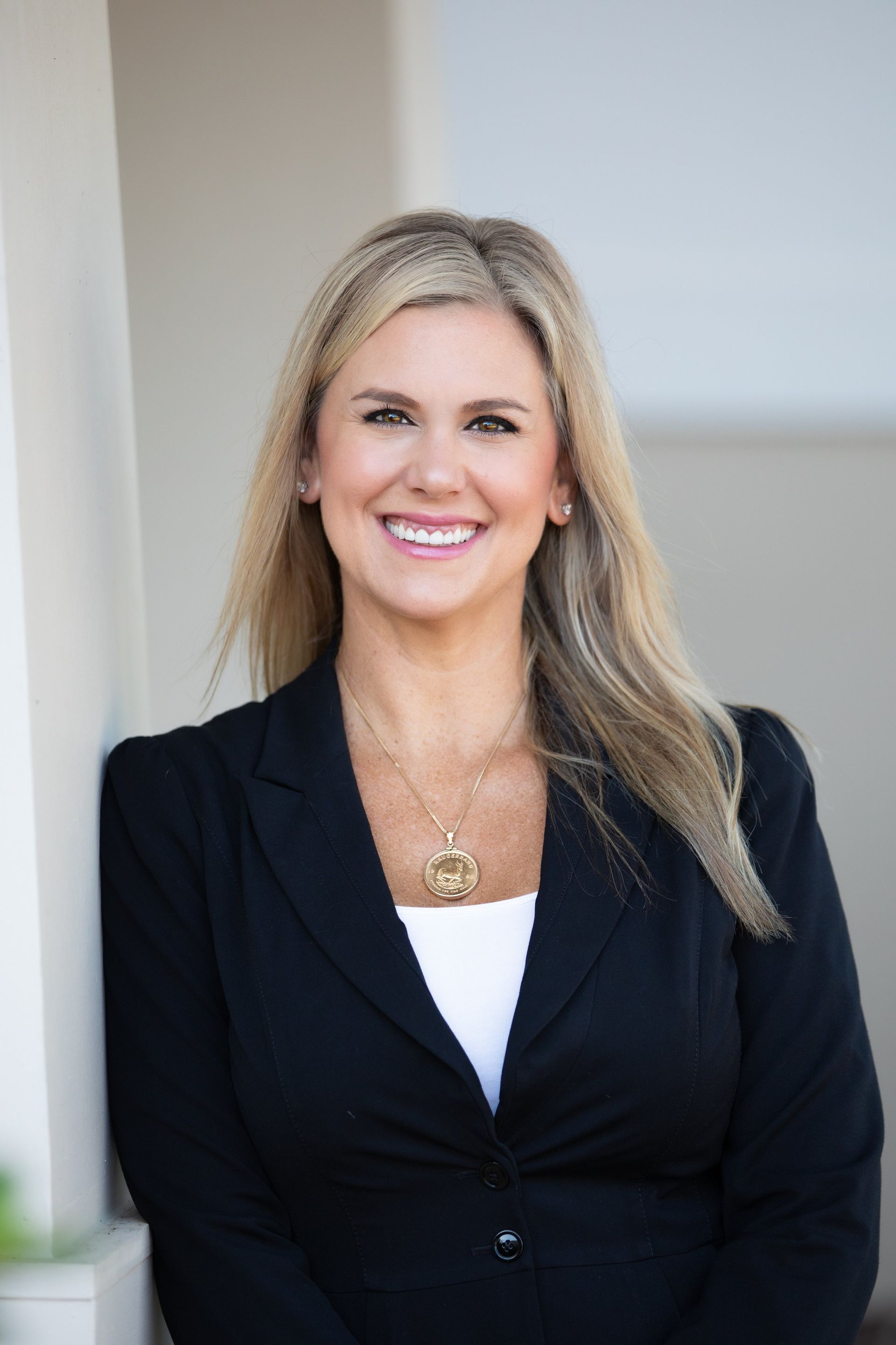 A woman in a black jacket and white shirt is smiling while leaning against a wall.