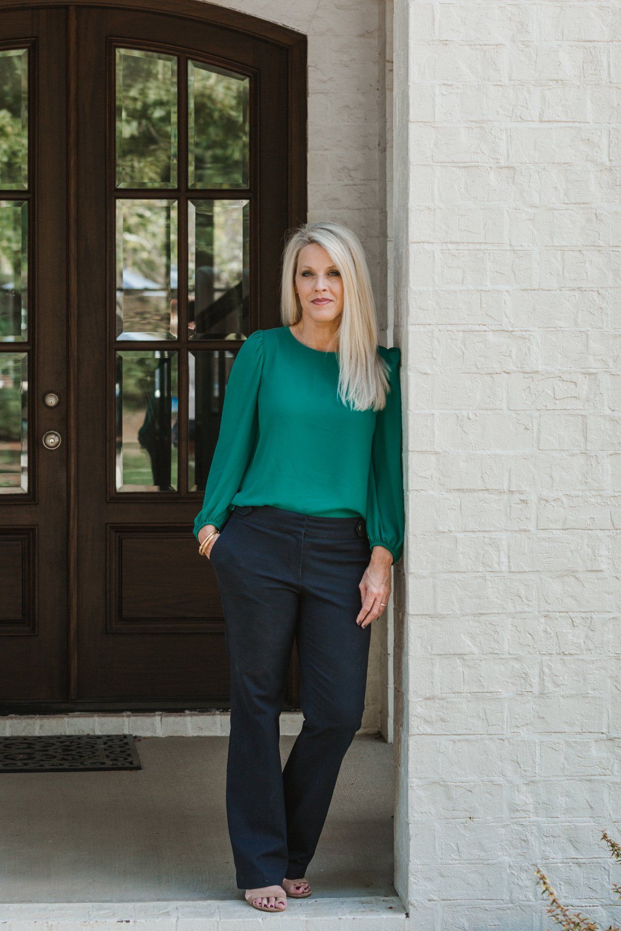 A woman in a green top and black pants is standing in front of a door.