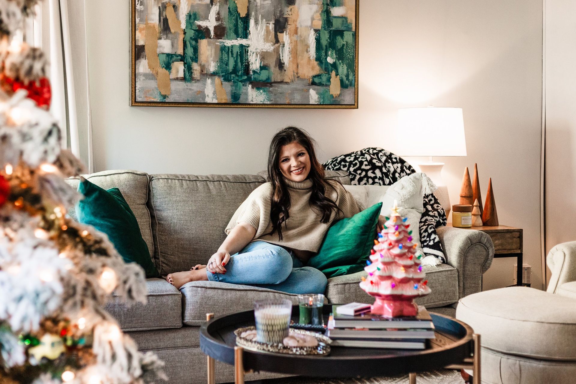 A woman is sitting on a couch in a living room with a christmas tree in the background.
