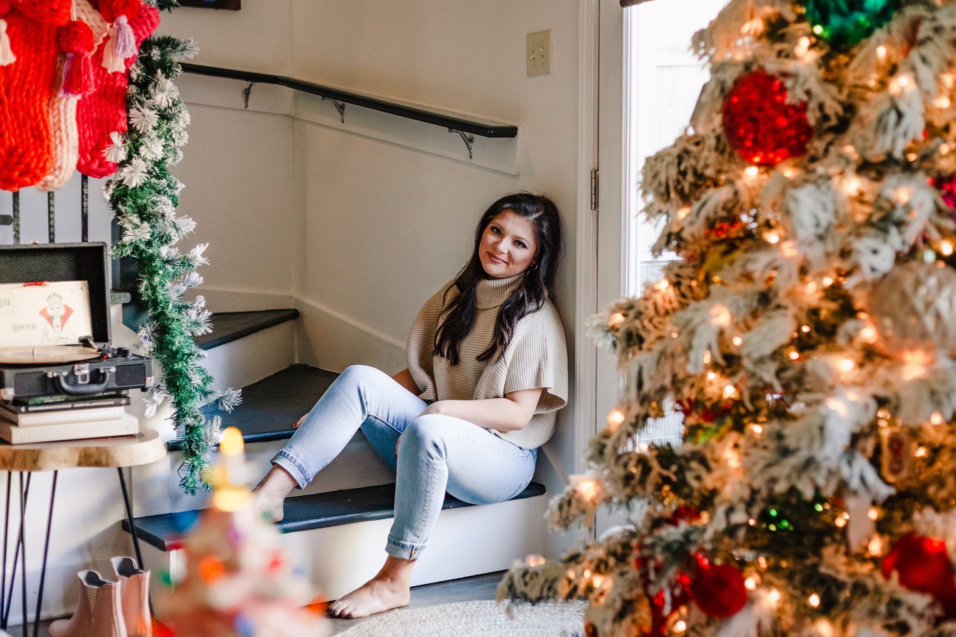 A woman is sitting on the stairs next to a christmas tree.