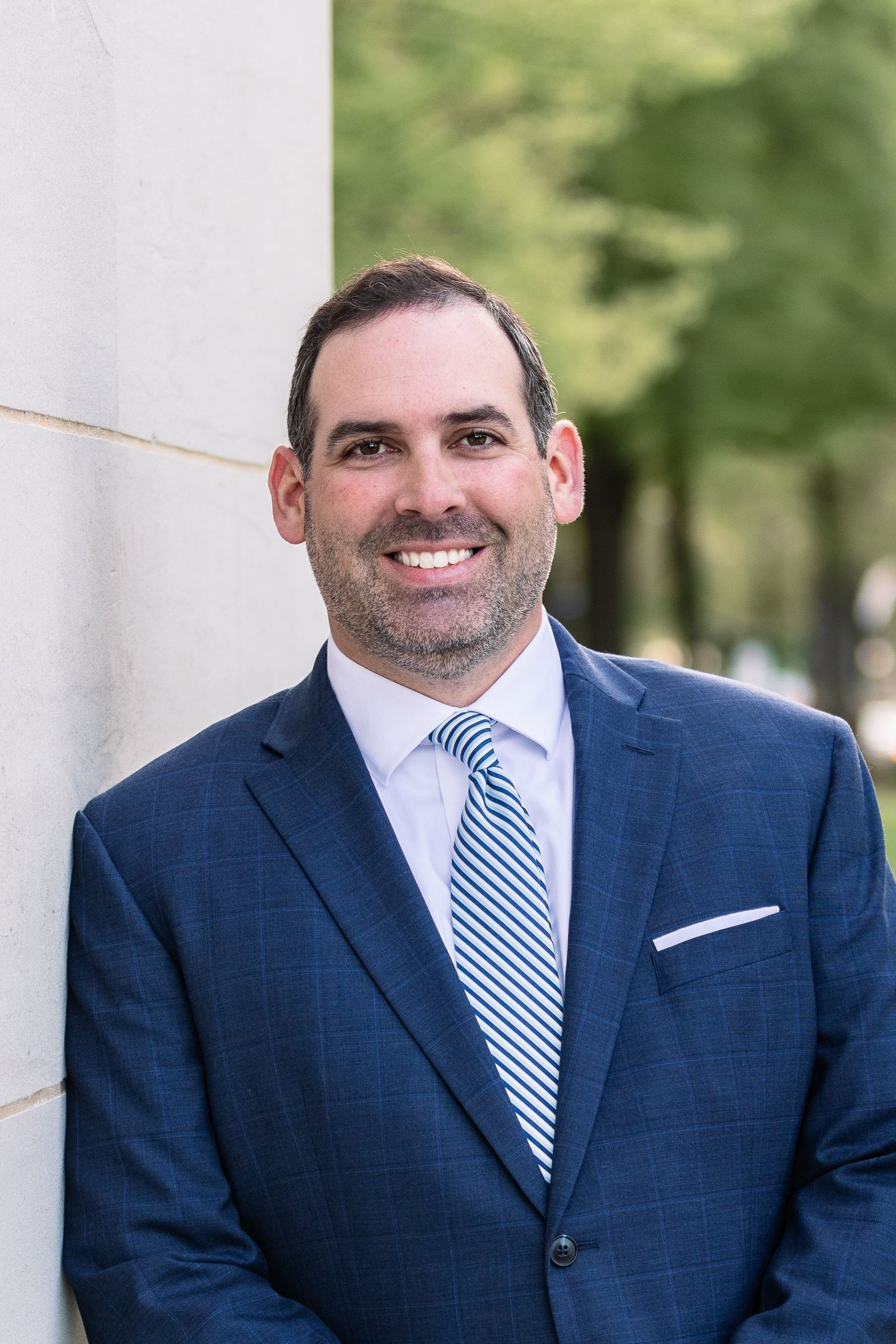 A man in a suit and tie is leaning against a wall and smiling.
