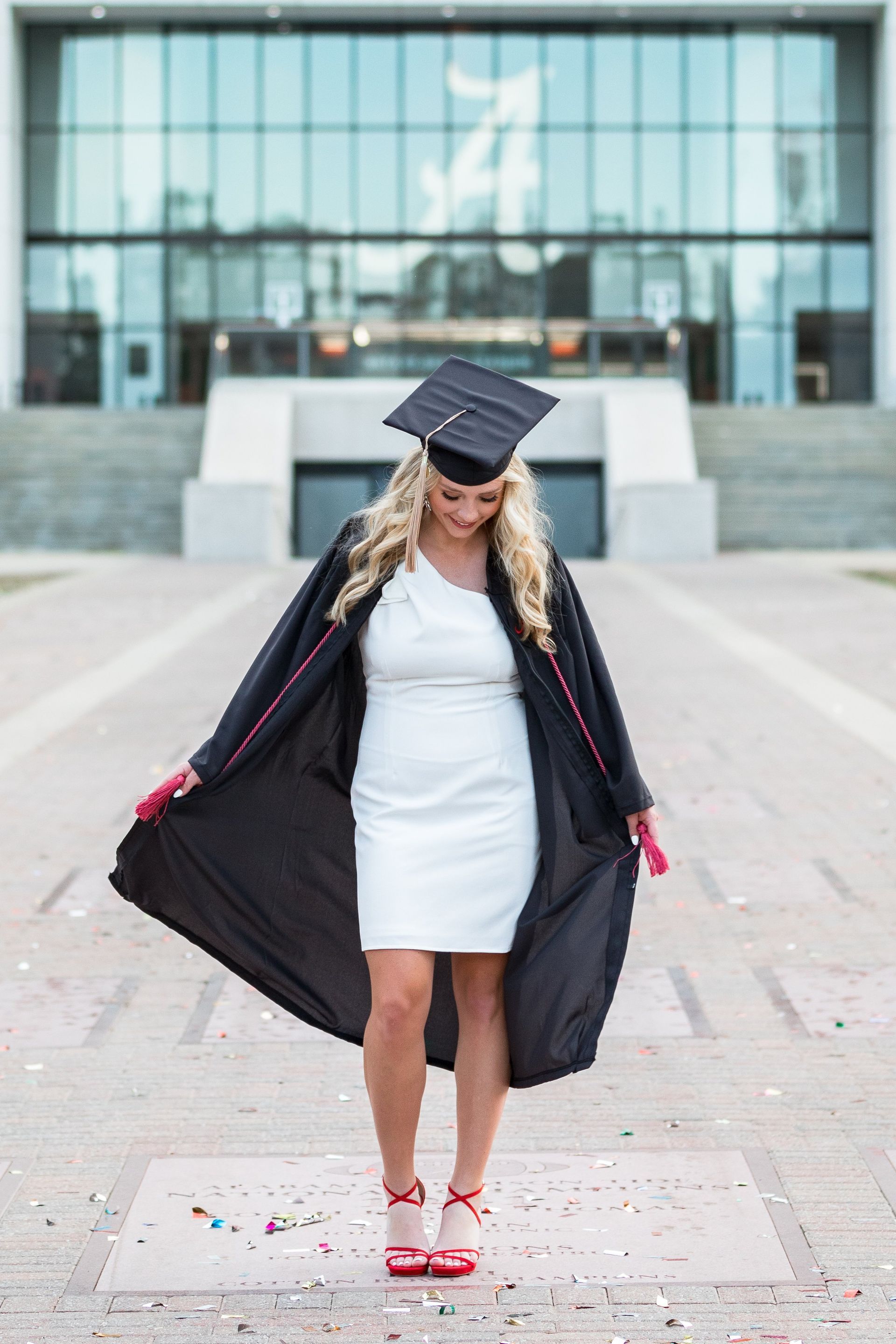 A woman in a graduation cap and gown is standing in front of a building.