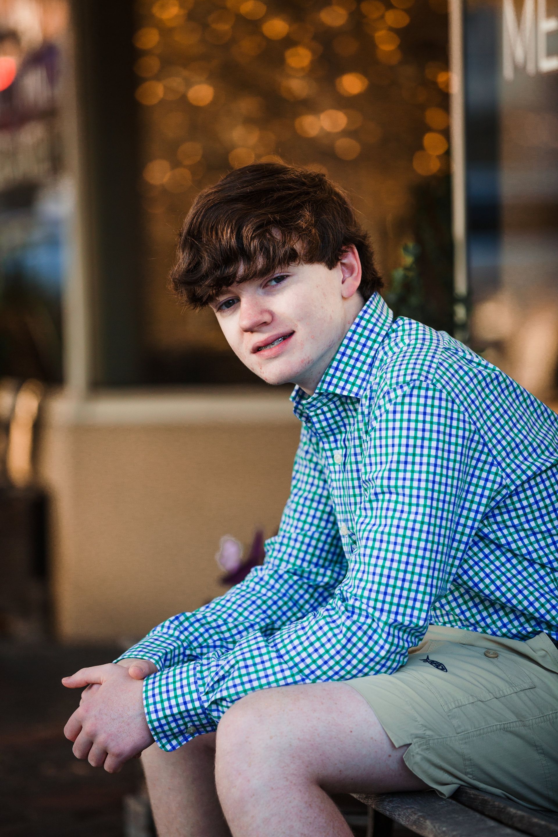 A young man is sitting on a bench in front of a building.