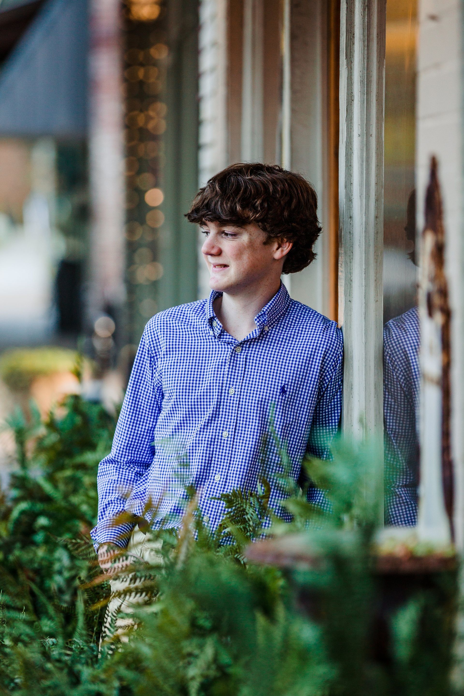 A young man in a blue shirt is leaning against a window.