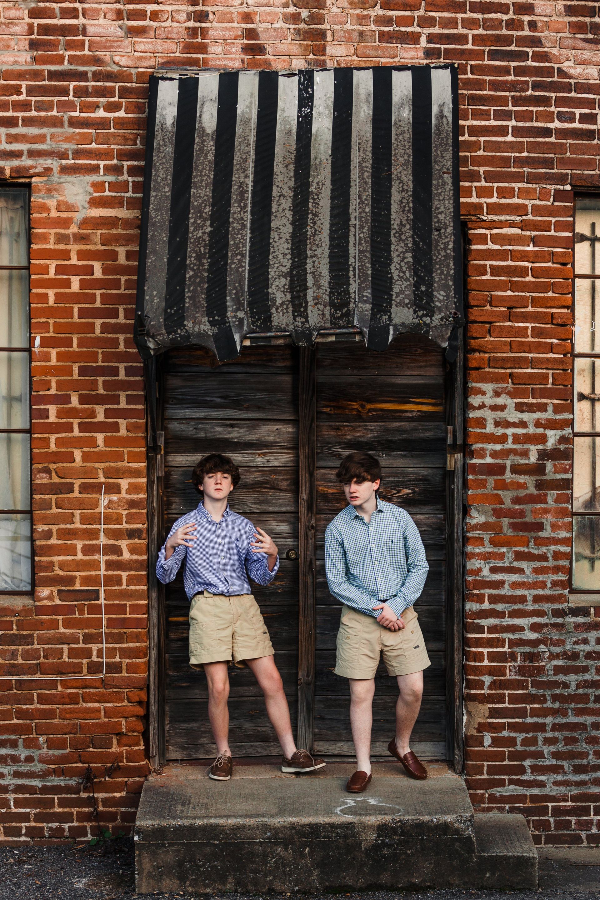 Two young boys are standing in front of a brick building.