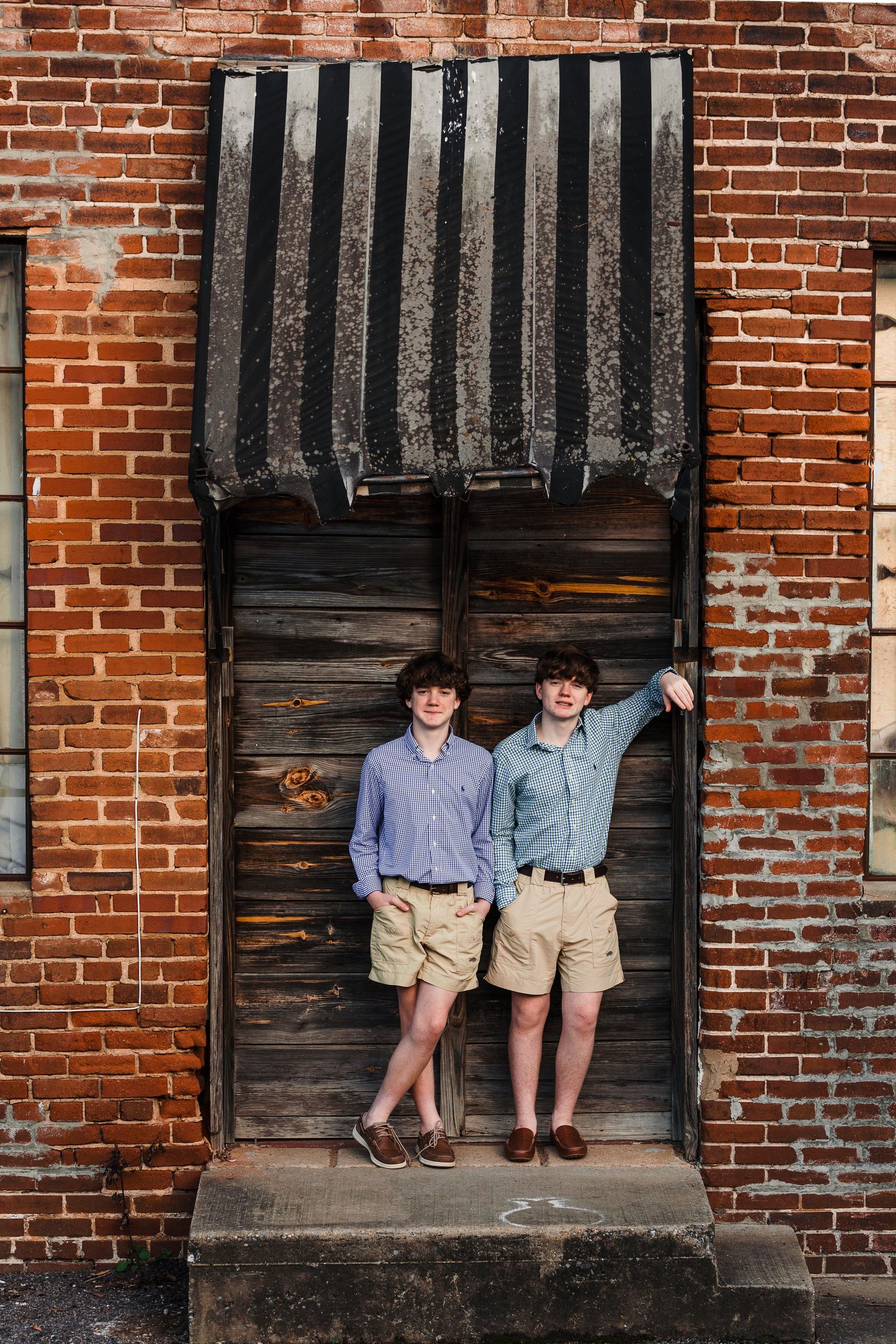 Two young boys are standing in front of a brick building.