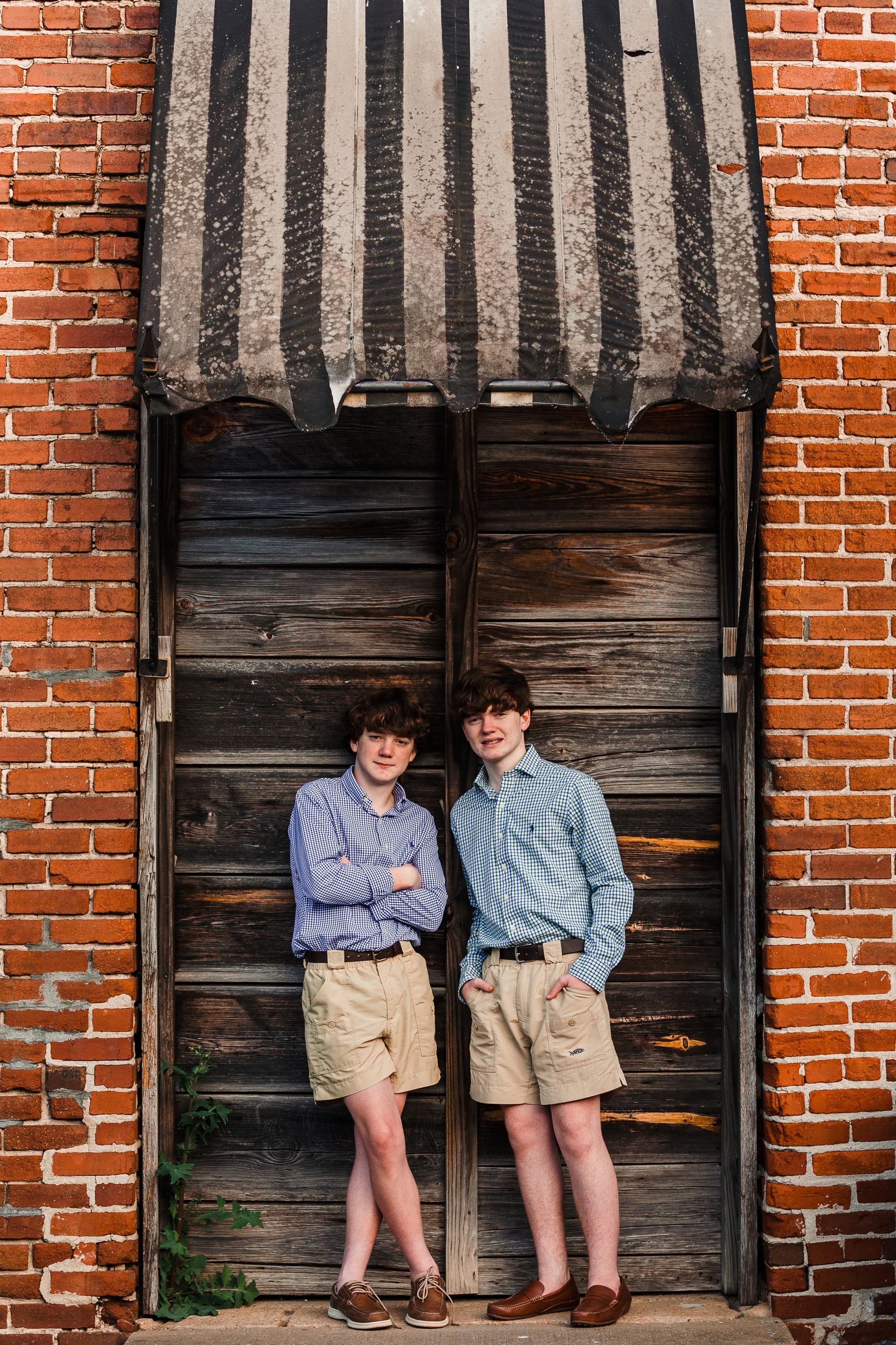 Two boys are standing next to each other in front of a wooden door.