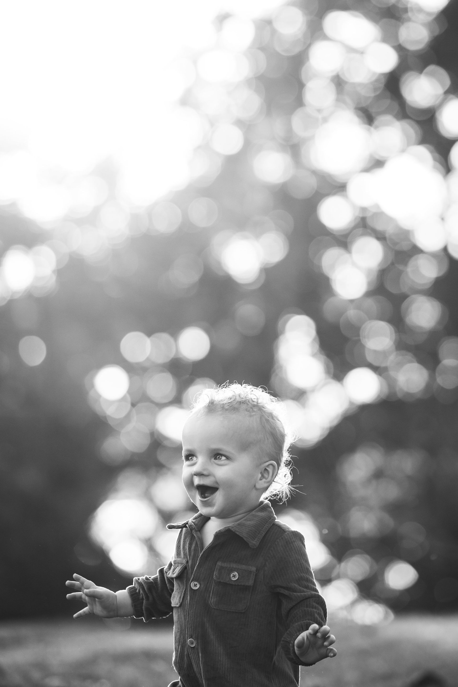 A black and white photo of a little boy standing in the grass.