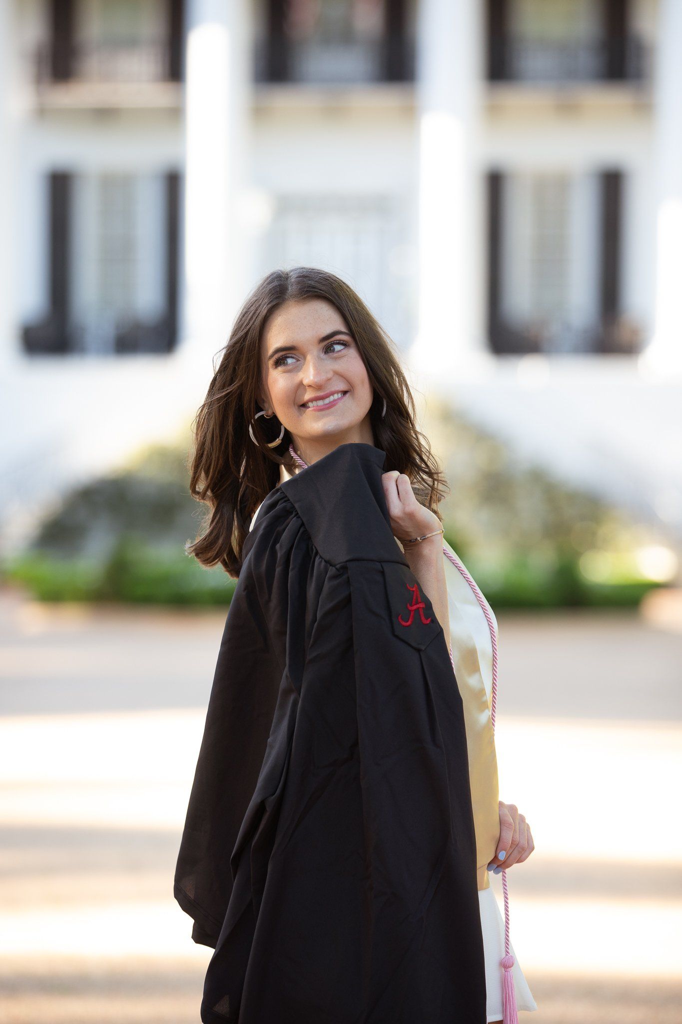 A woman in a graduation cap and gown is standing in front of a white building.