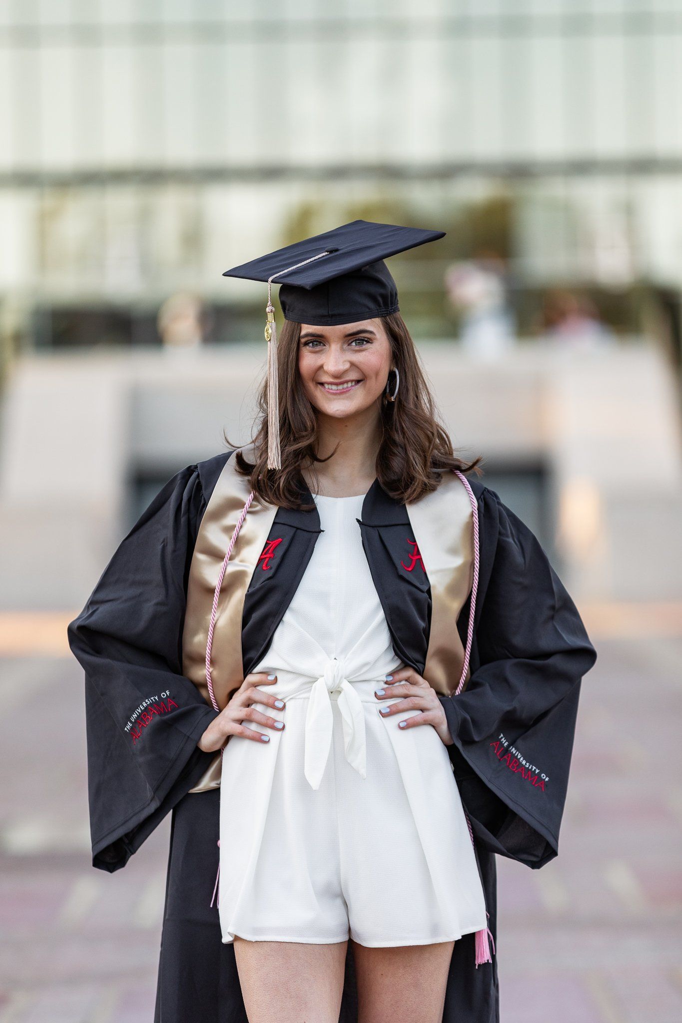 A woman in a graduation cap and gown is standing in front of a building.