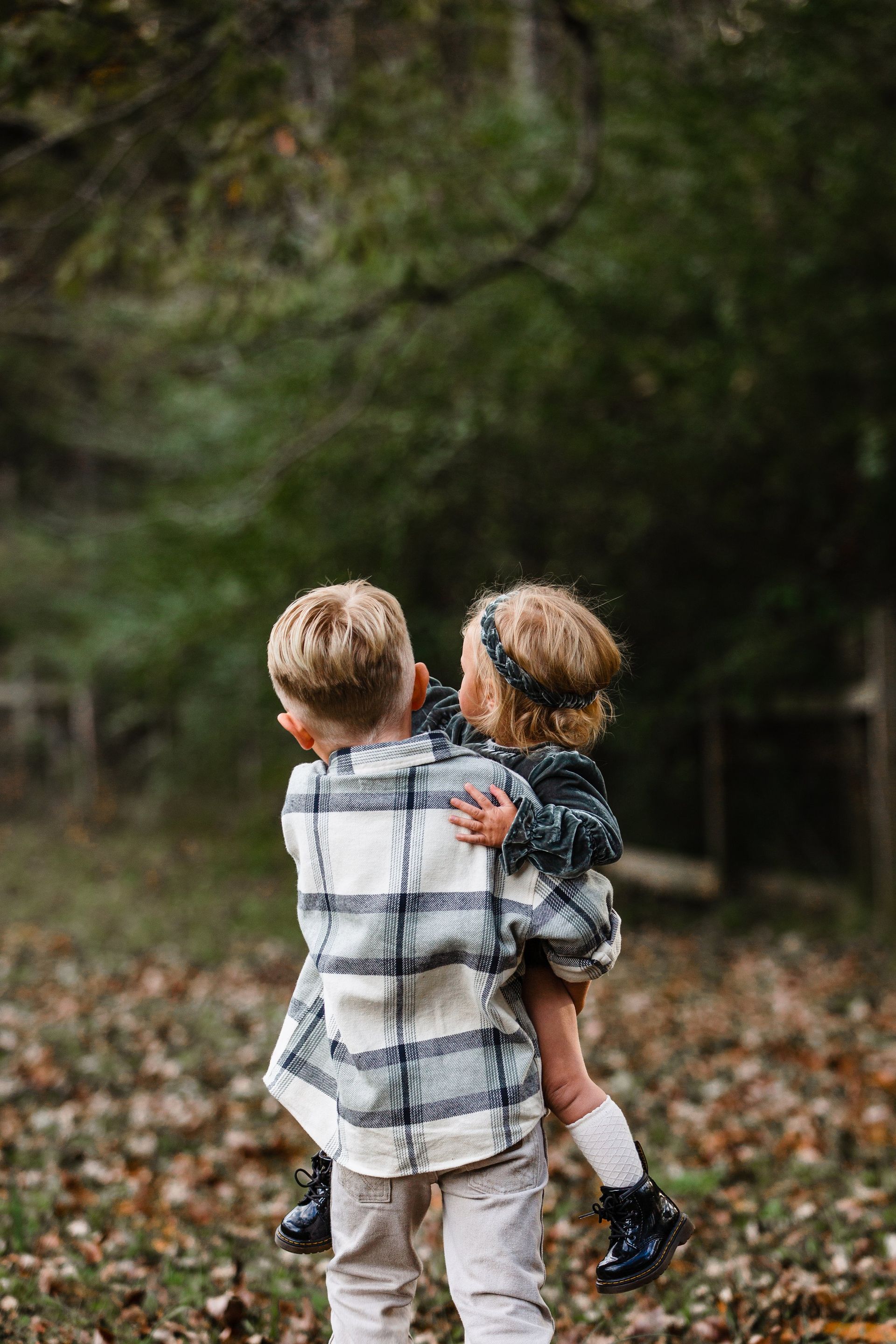 A boy is carrying a little girl on his shoulders in the woods.