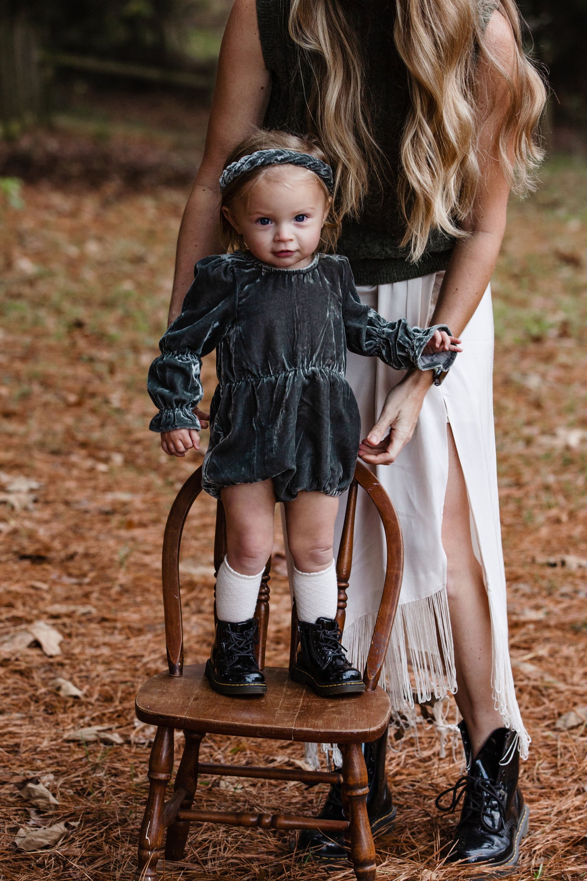 A woman is standing next to a little girl sitting on a chair.