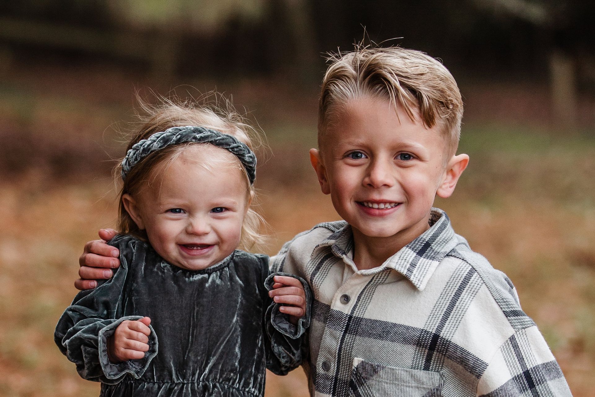 A boy and a girl are posing for a picture in the woods.