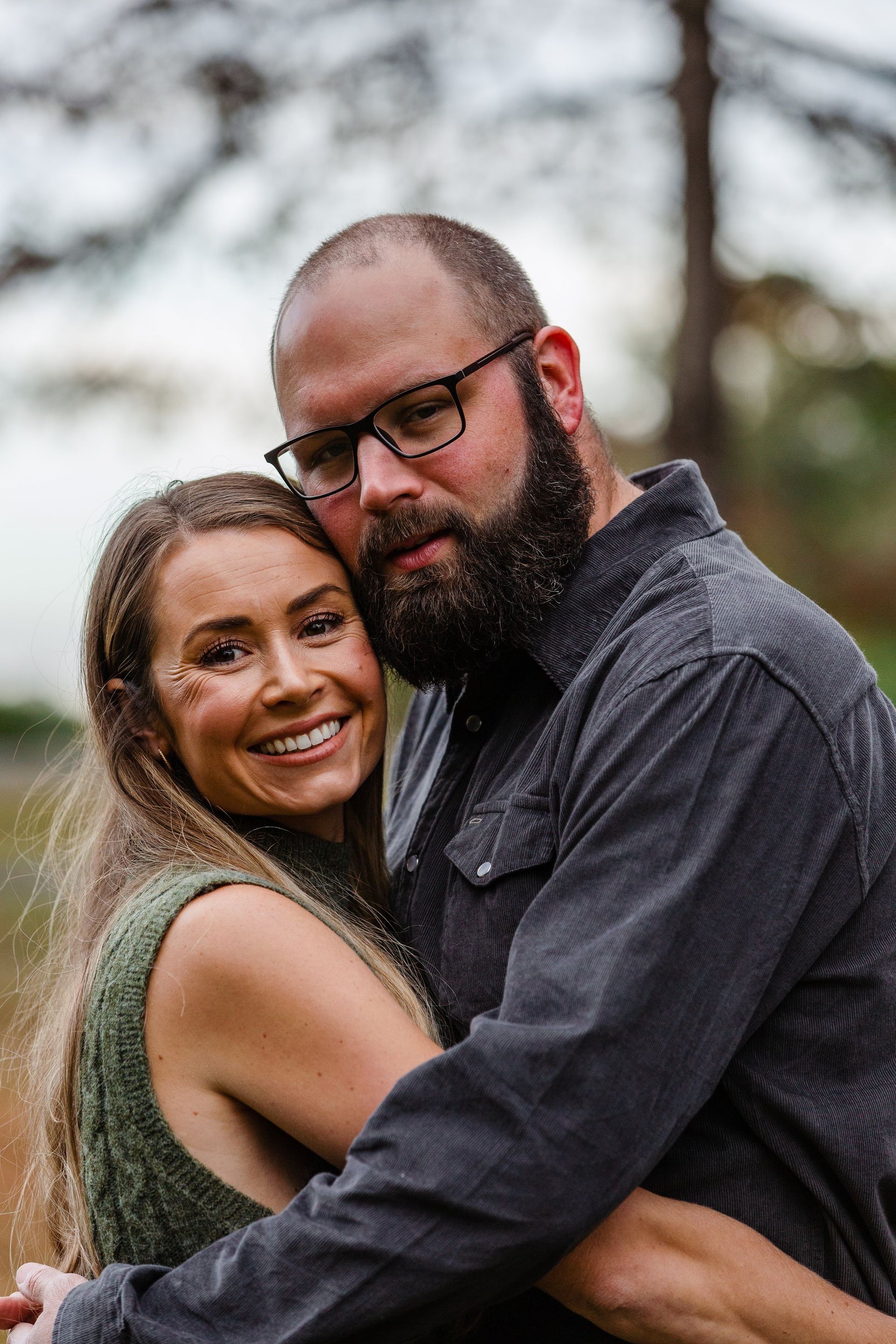 A man with a beard and glasses is hugging a woman.