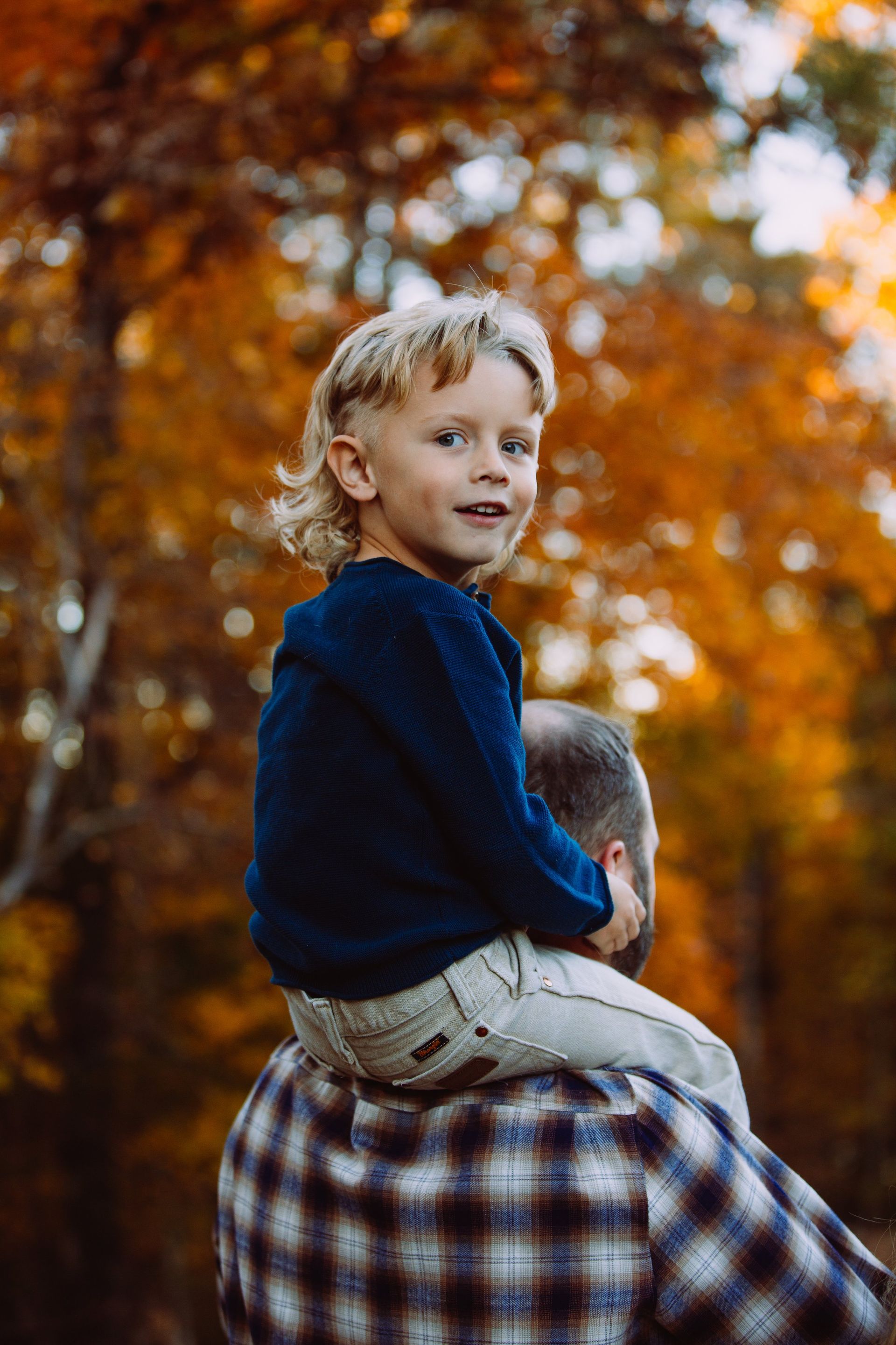 A little boy is sitting on a man 's shoulders in the woods.