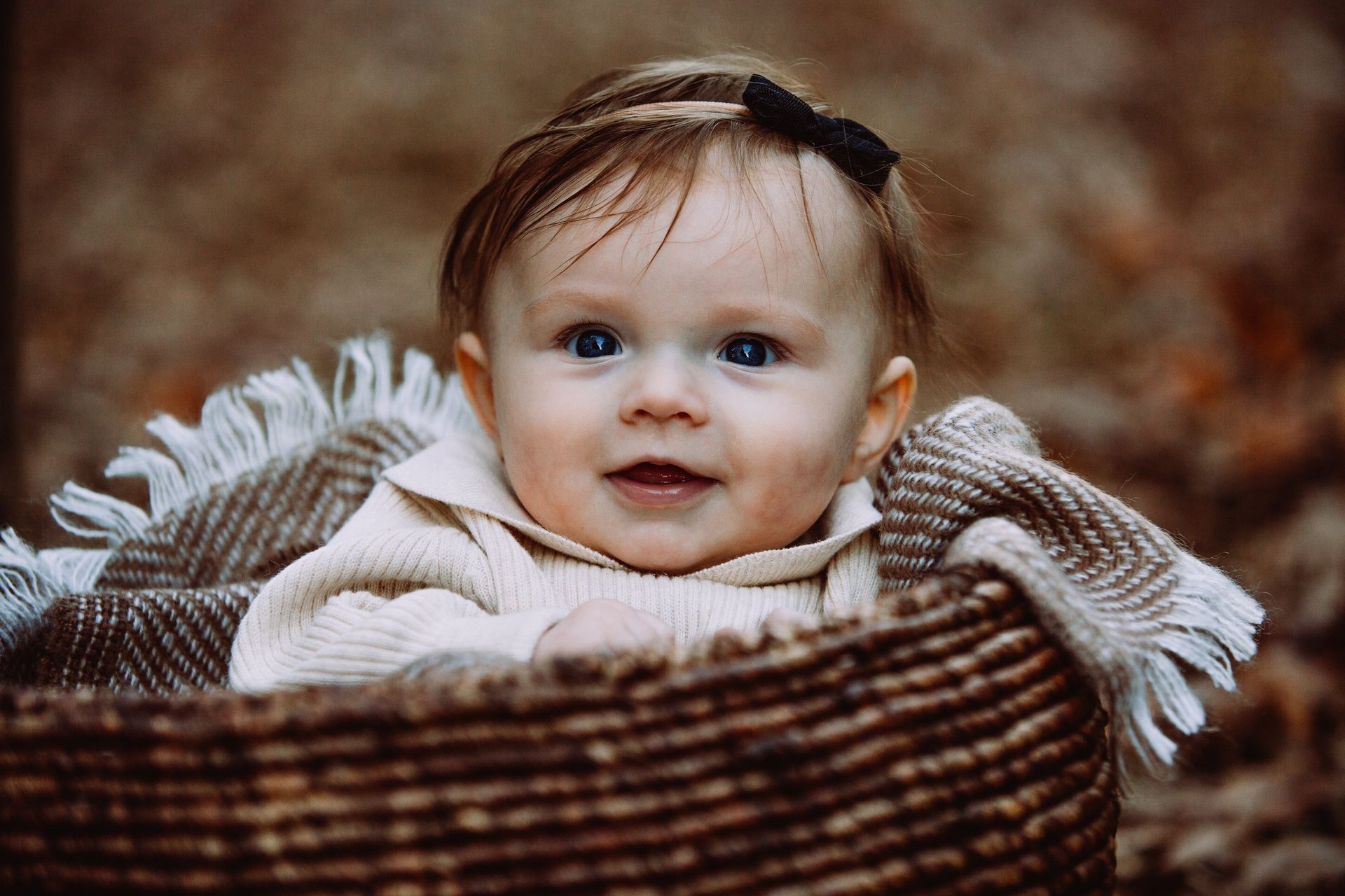 A baby girl is sitting in a wicker basket.