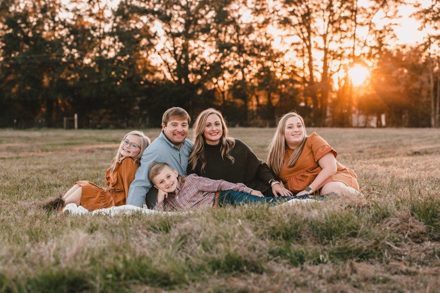 A family is laying on a blanket in a field at sunset.