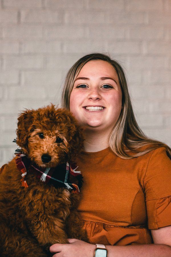 A woman is holding a small brown dog in her arms.