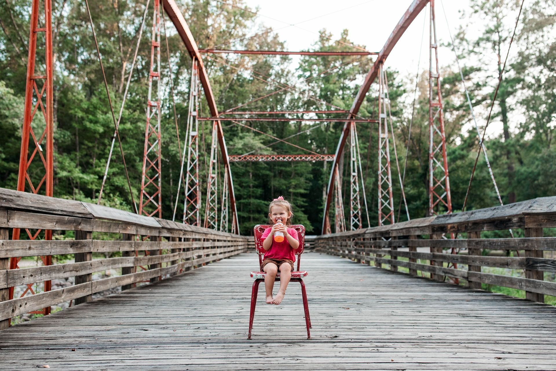 A little girl is sitting in a red chair on a wooden bridge.