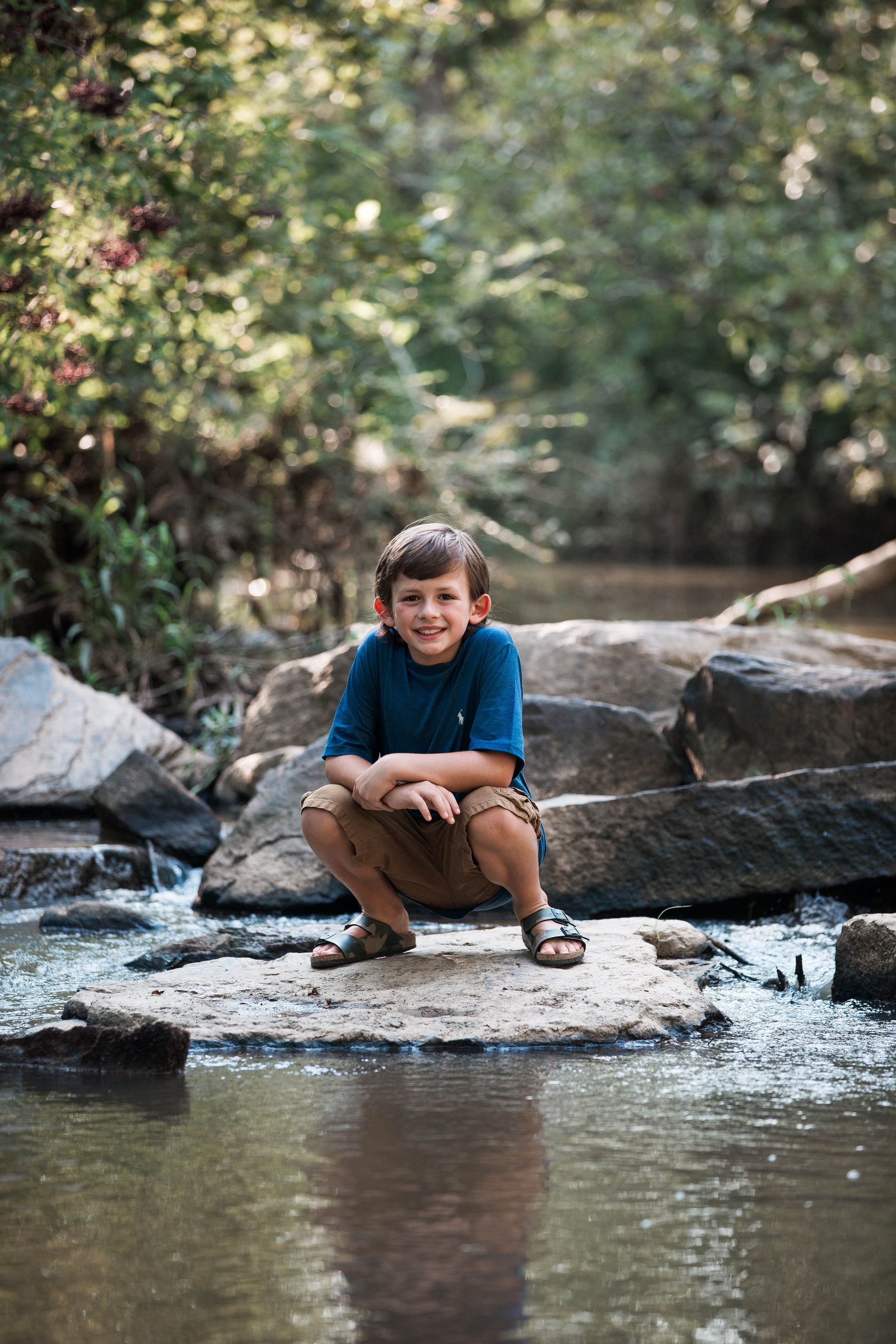 A young boy is sitting on a rock in the middle of a river.