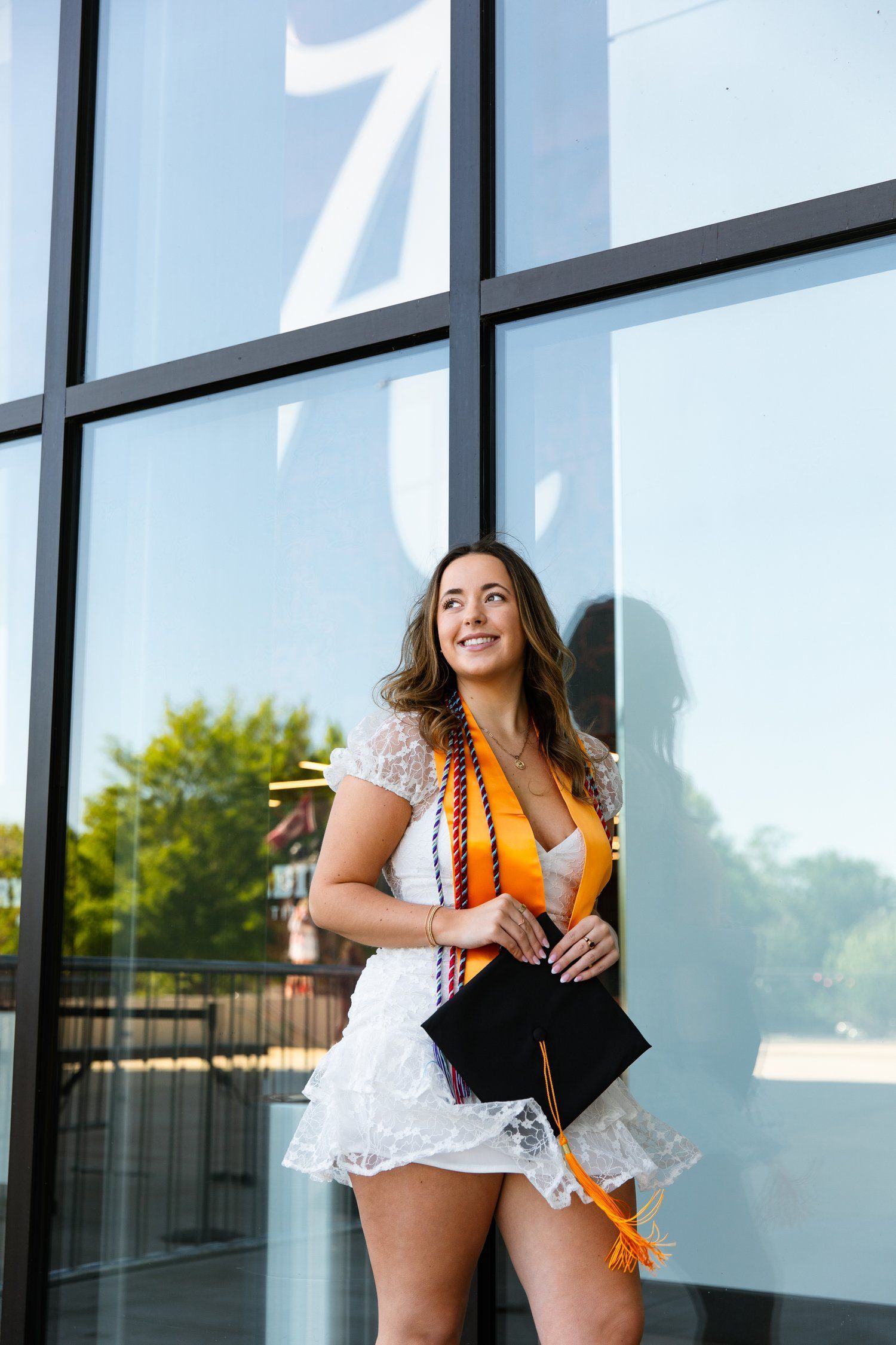 A woman in a graduation cap and gown is standing in front of a building.