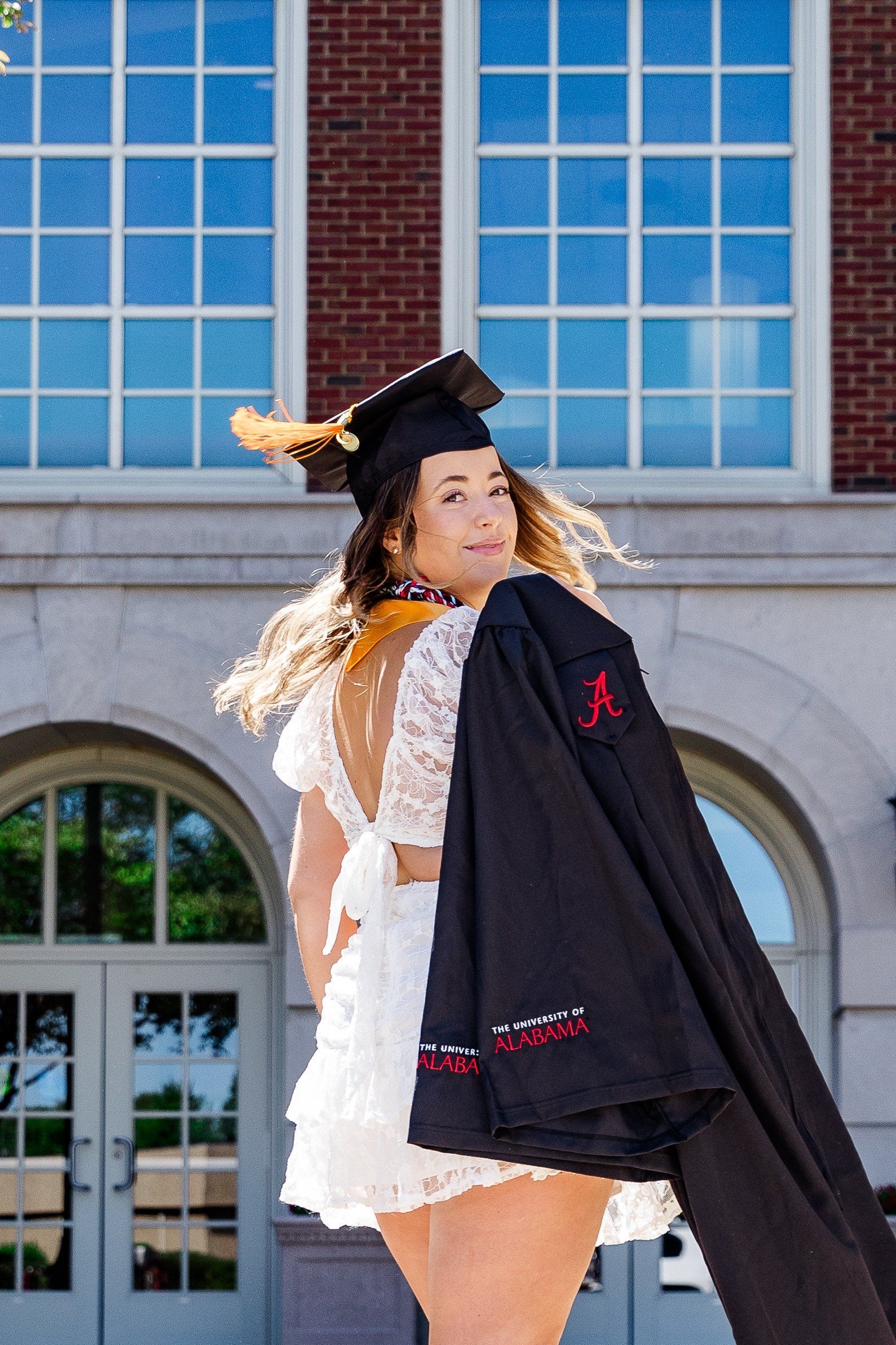 A woman in a graduation cap and gown is standing in front of a building.