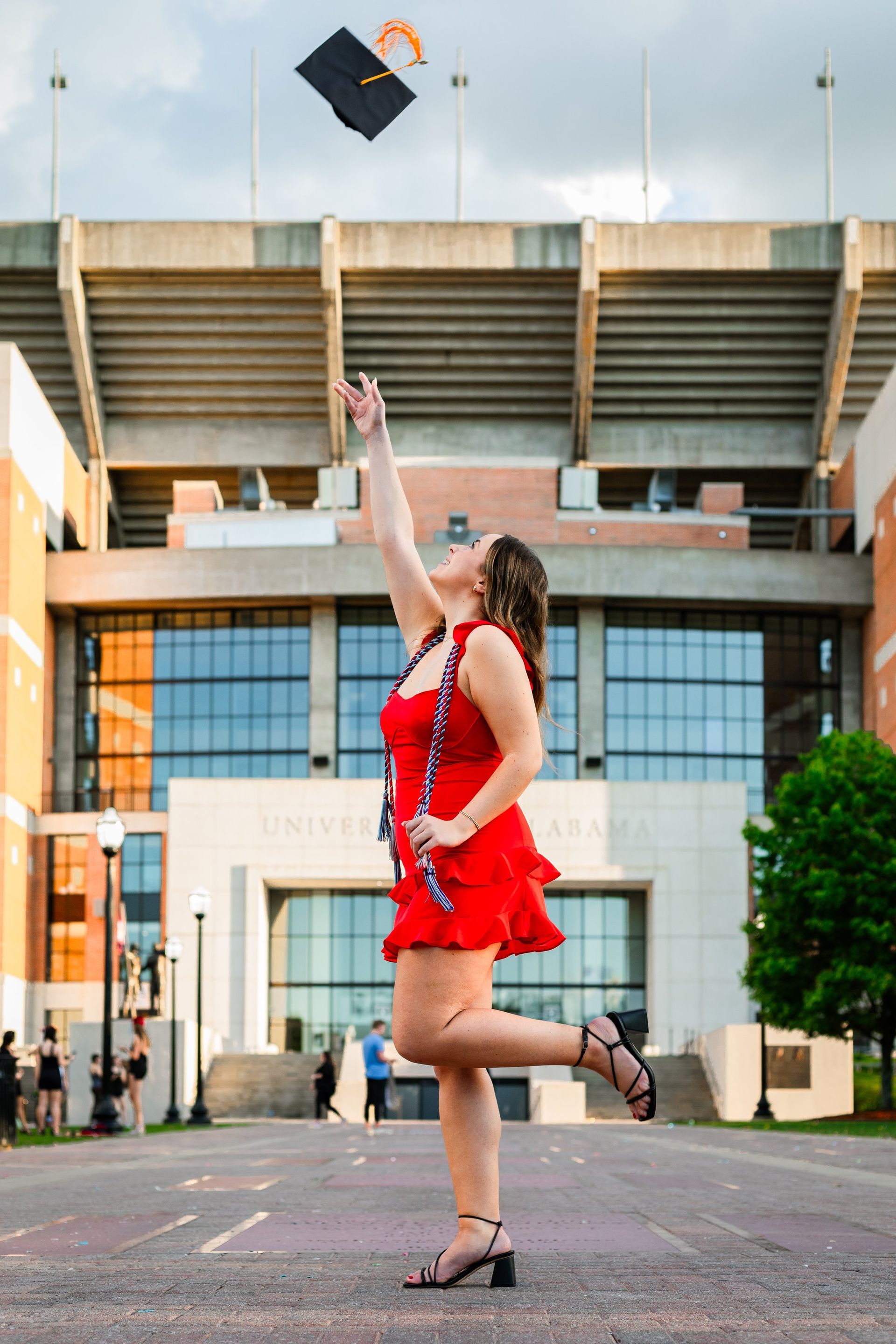 A woman in a red dress is throwing her graduation cap in the air.
