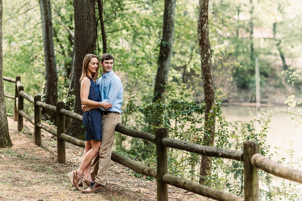 A man and a woman are standing next to a wooden fence in the woods.