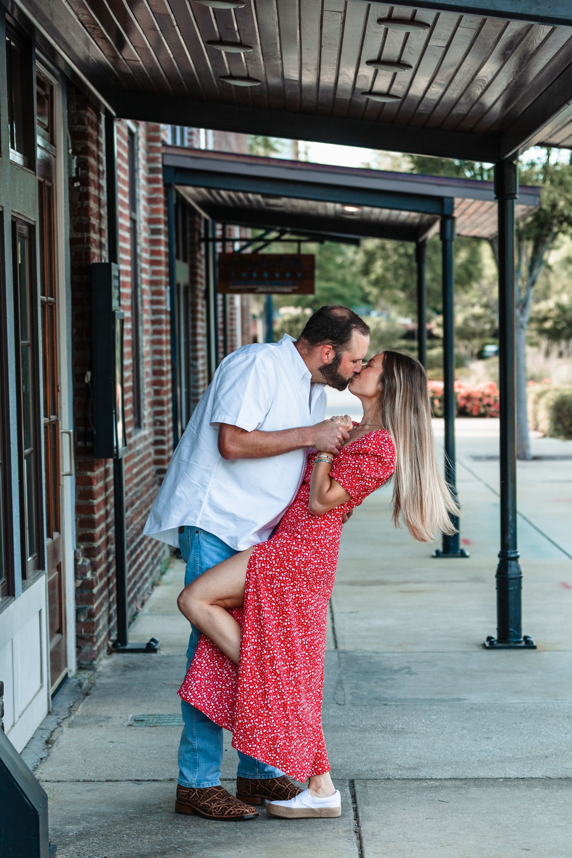 A man is holding a woman in his arms and kissing her on the sidewalk.
