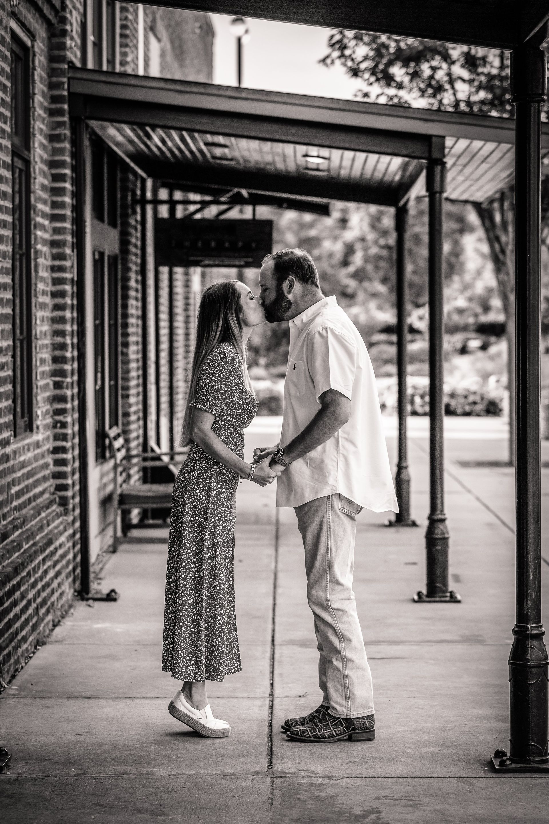 A black and white photo of a man and a woman holding hands on a sidewalk.