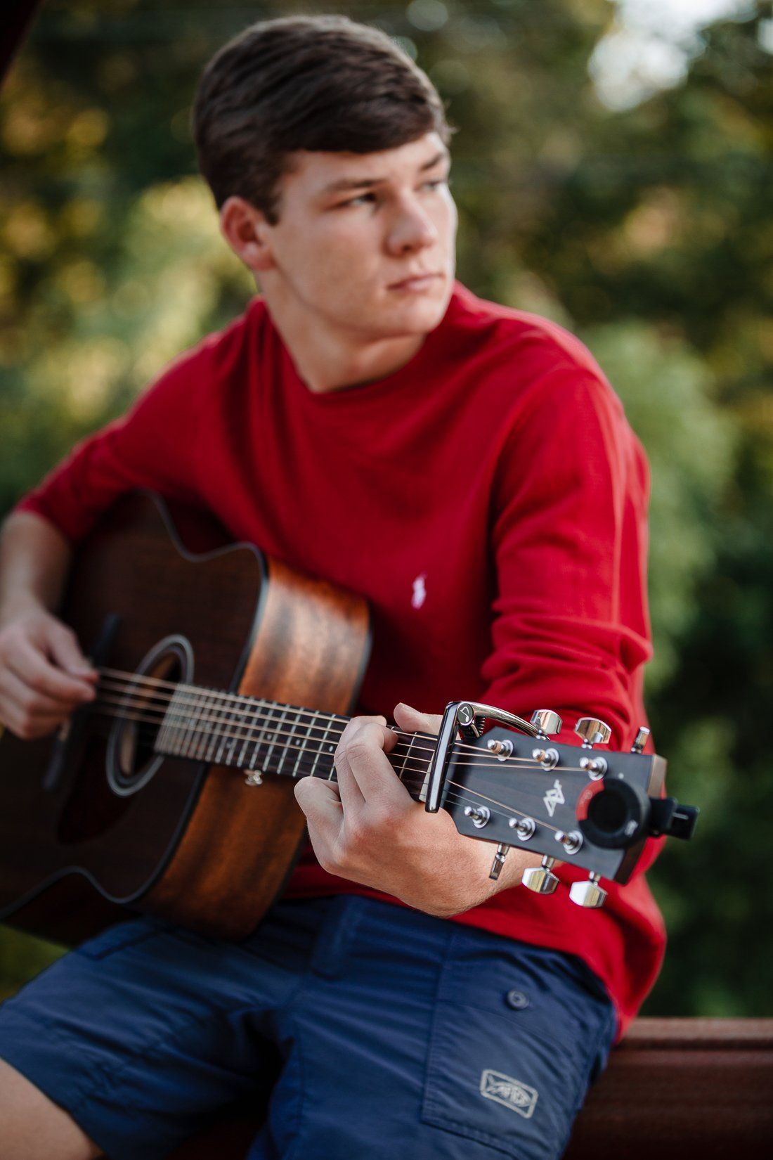 A young man in a red sweater is playing an acoustic guitar.