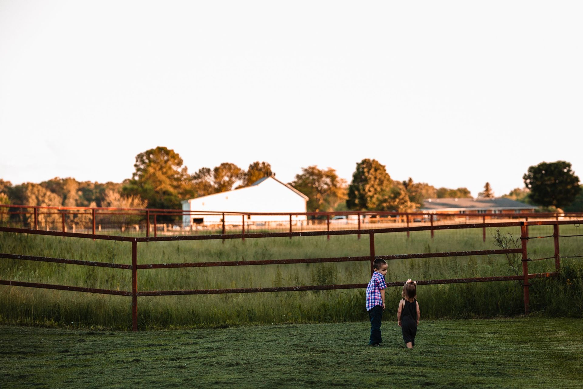 A boy and a girl are standing next to a fence in a field.
