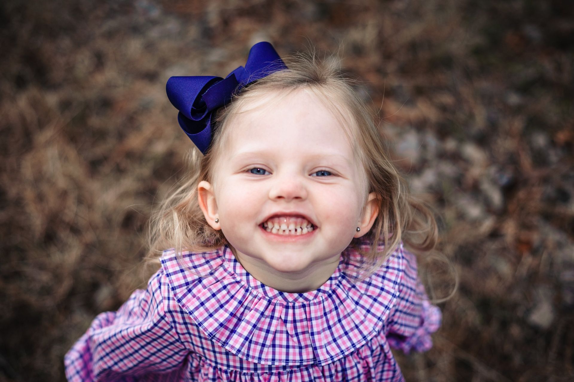 A little girl wearing a purple dress and a purple bow is smiling.