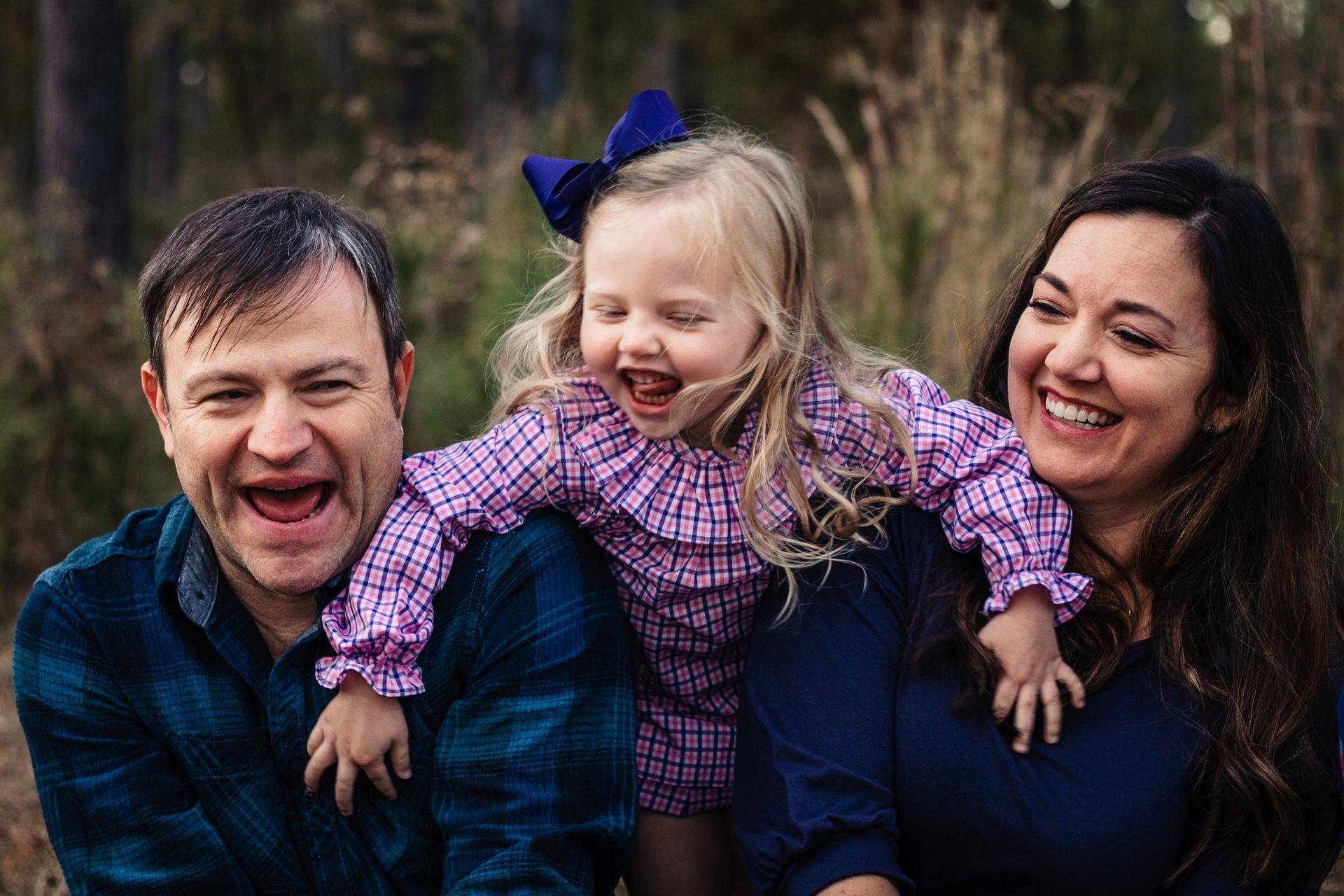 A man and woman are holding a little girl on their shoulders.