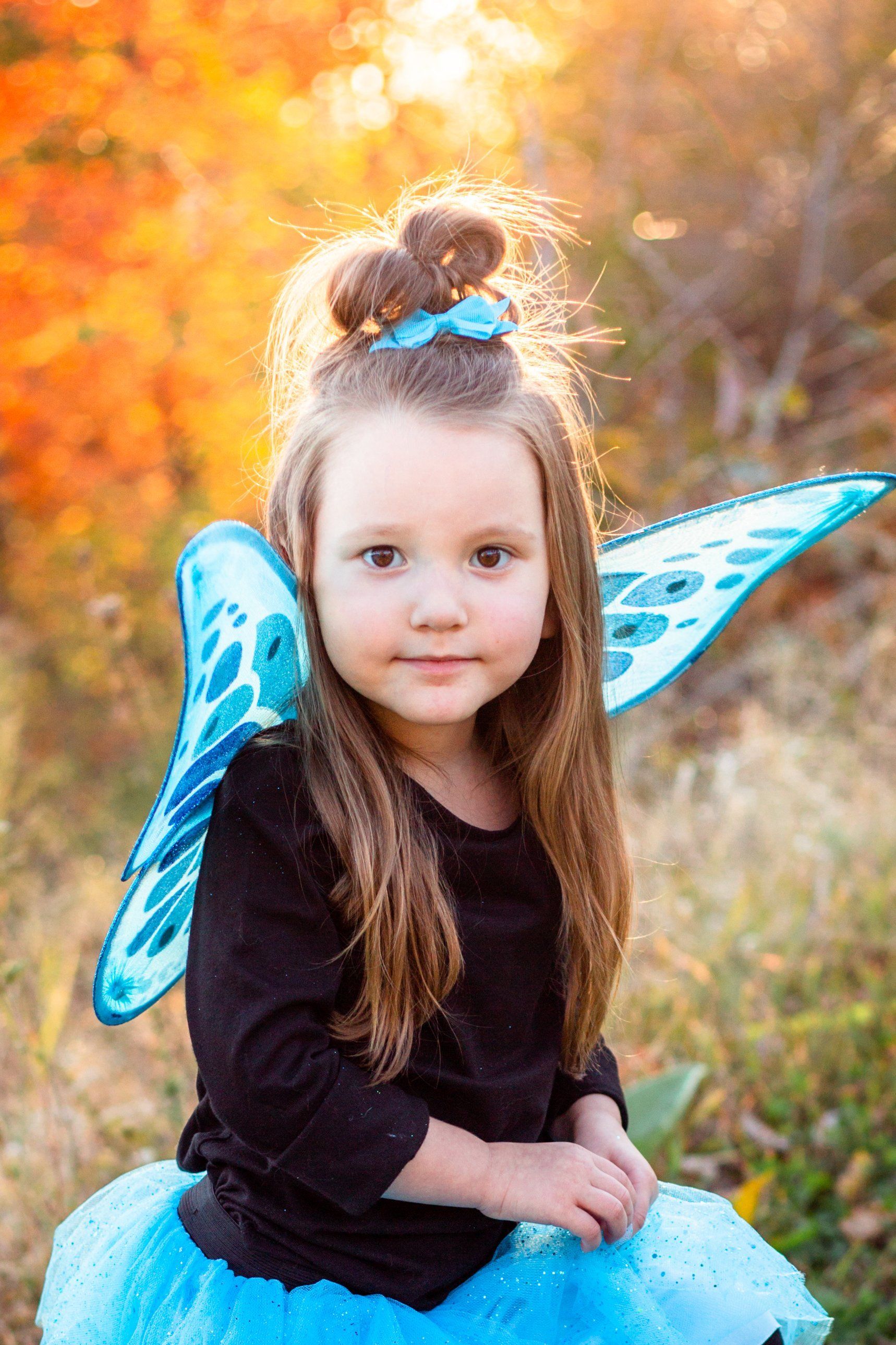 Young girl dressed in black wearing blue fairy wings.