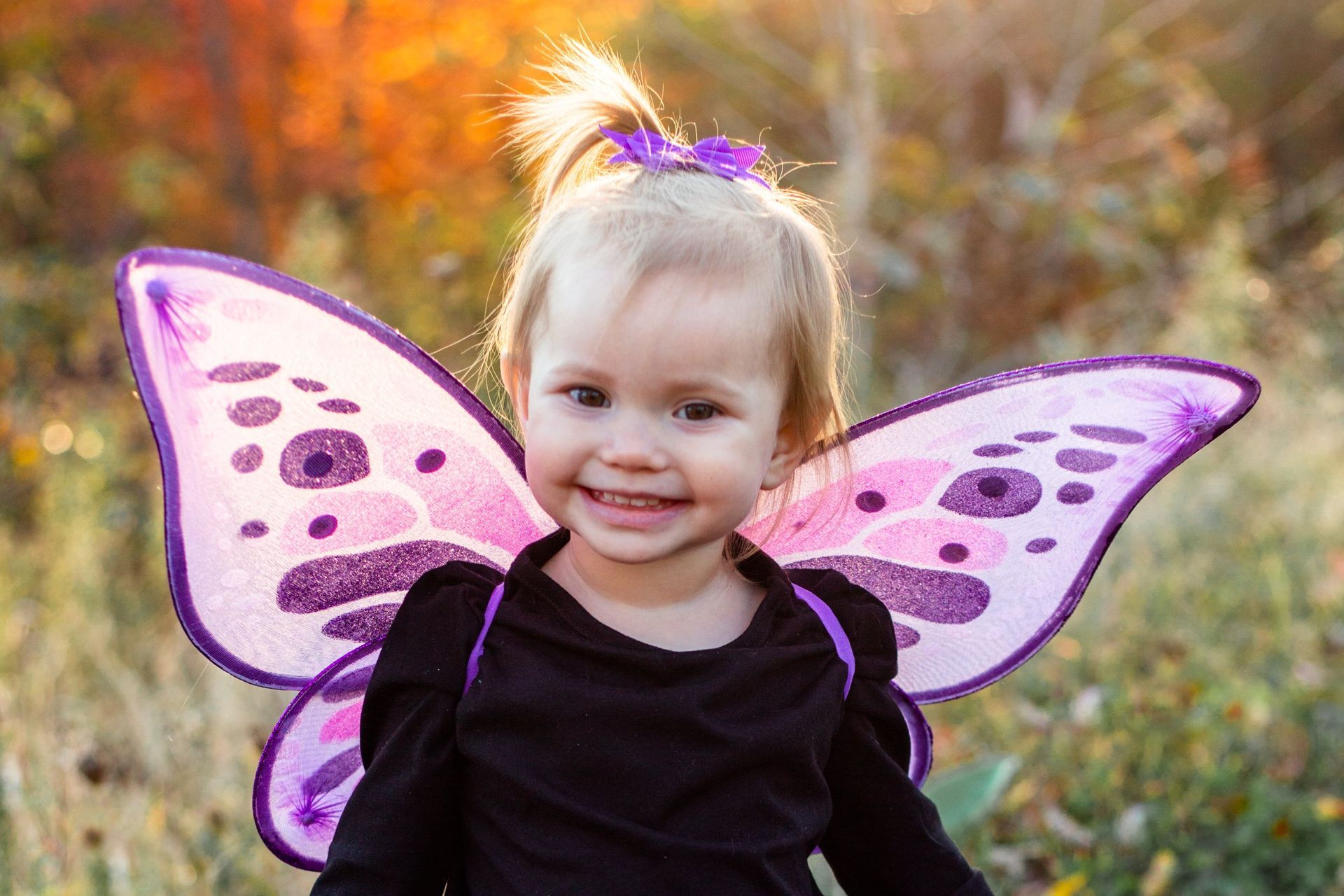 A little girl is dressed in a fairy costume with purple wings.