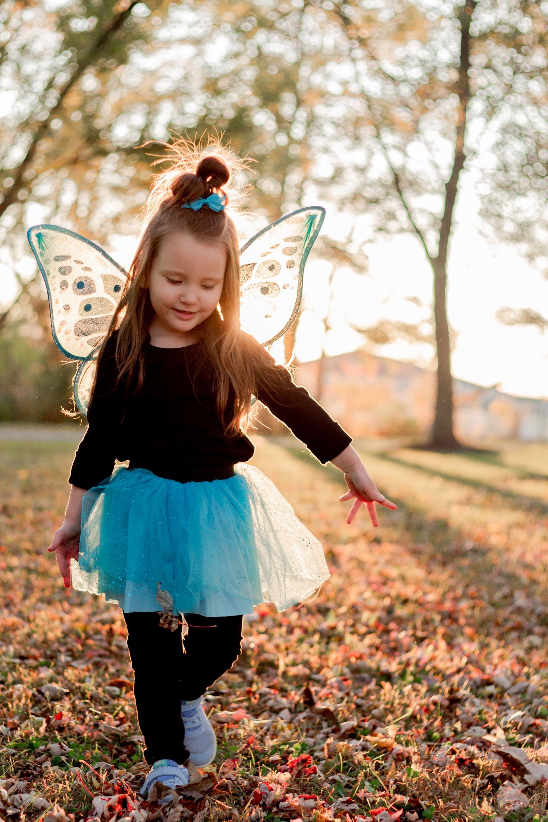 A little girl in a fairy costume is standing in the grass.