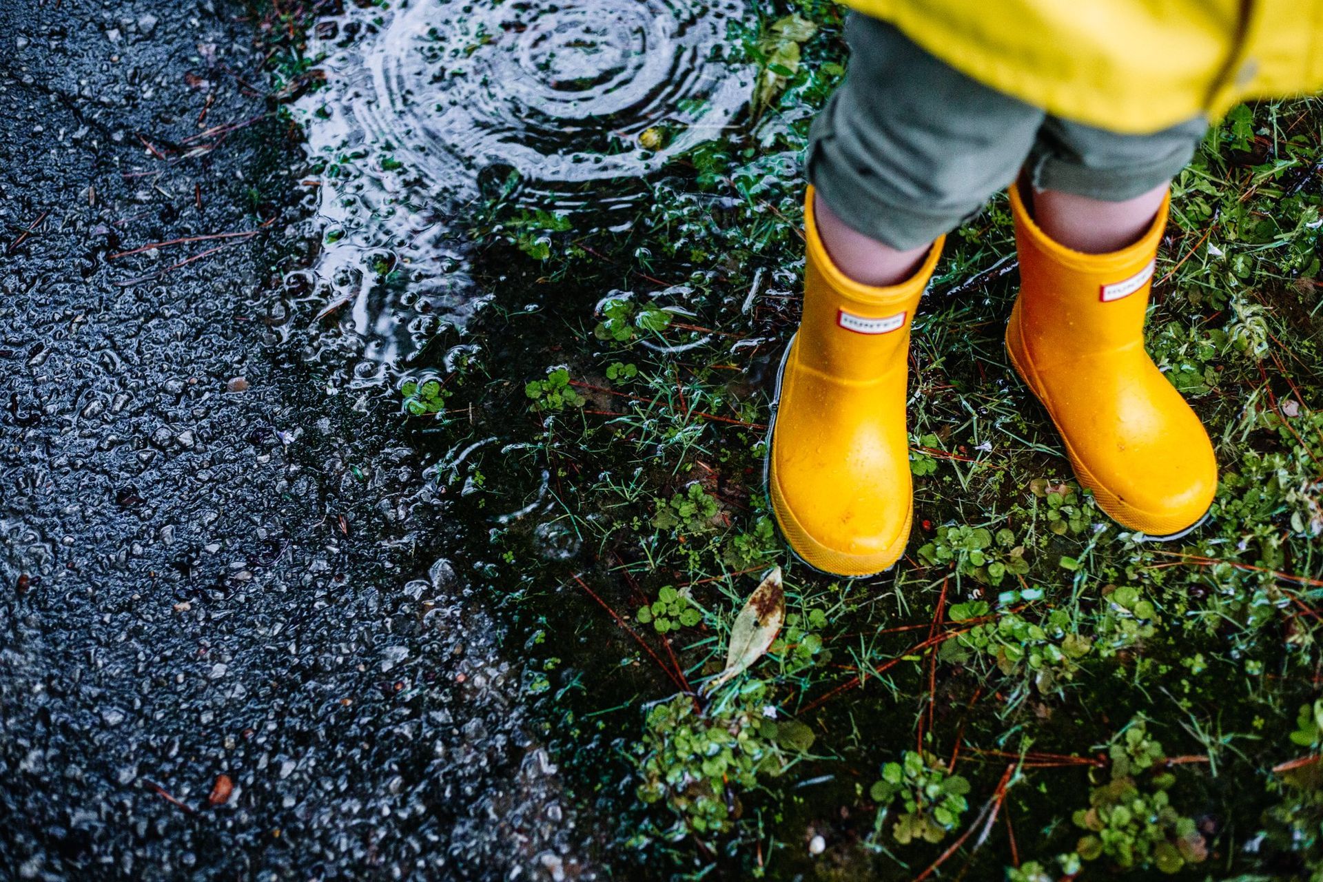A child wearing yellow rain boots is standing in a puddle.