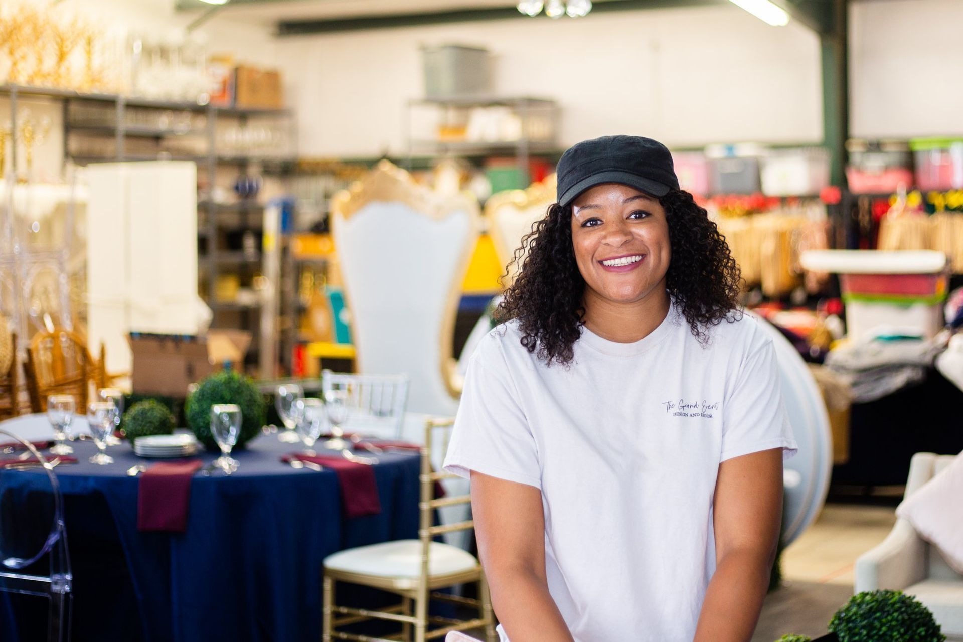 A woman is sitting in front of a table and chairs in a warehouse.