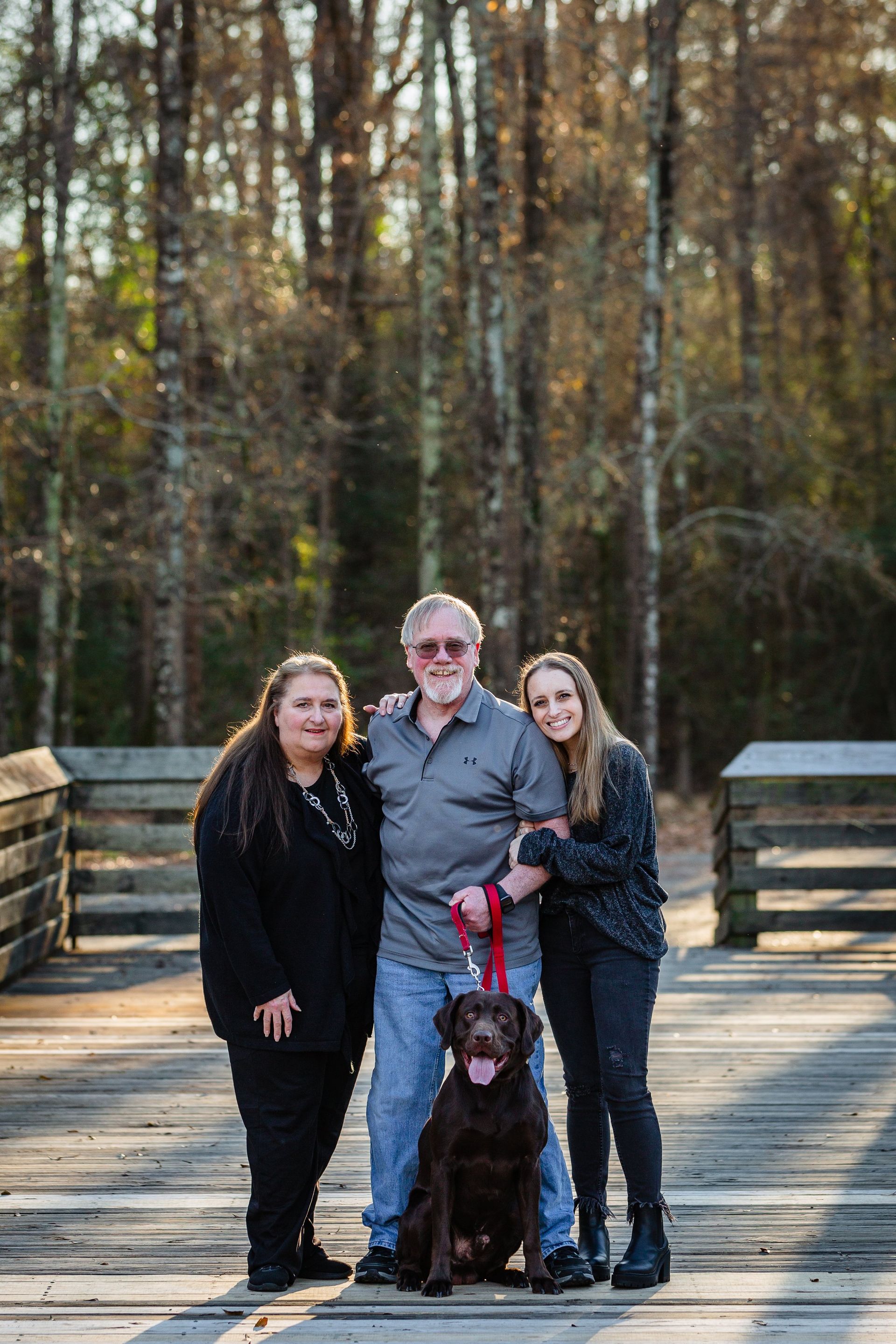 A family is posing for a picture with their dog on a bridge.