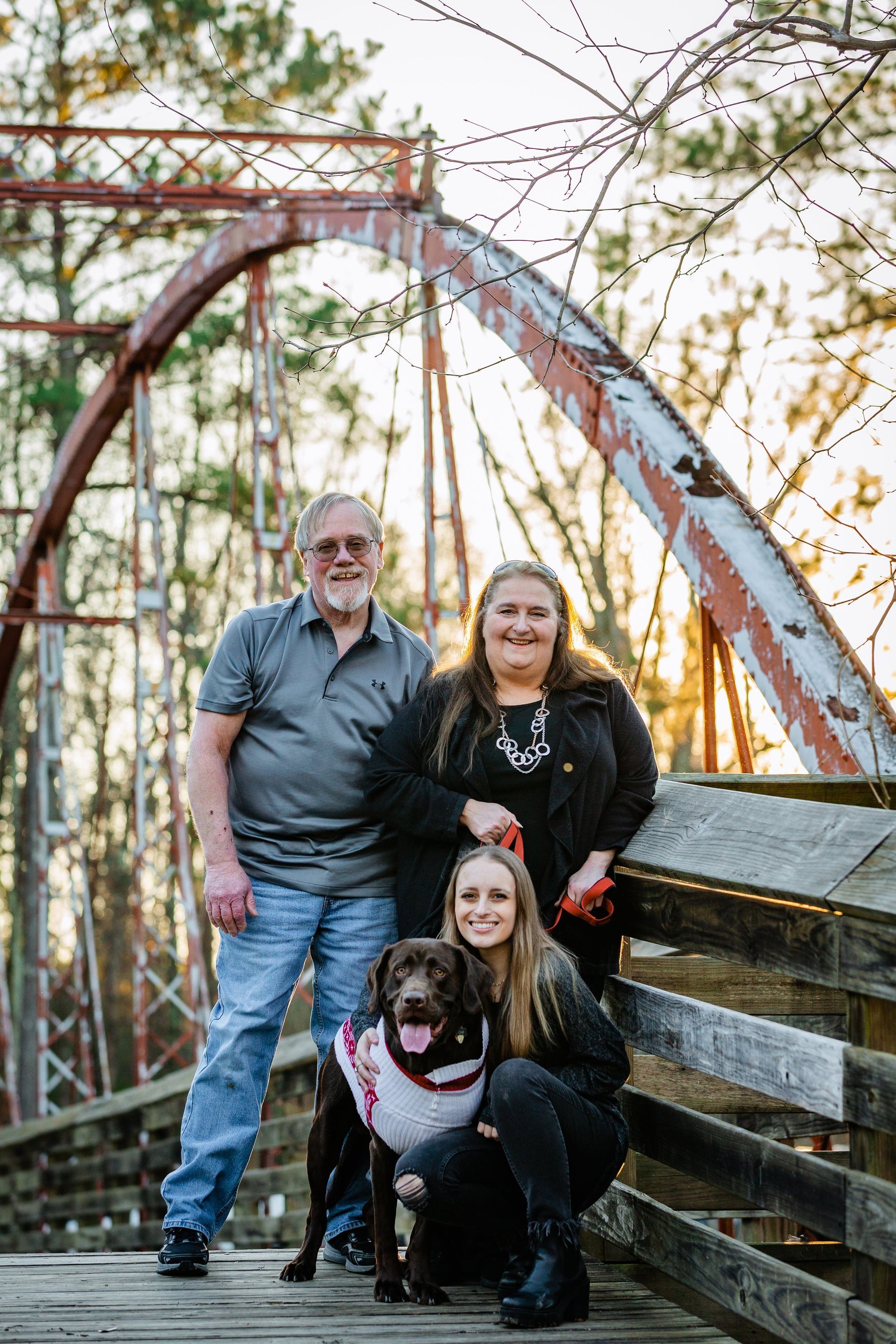 A family is posing for a picture with their dog on a bridge.