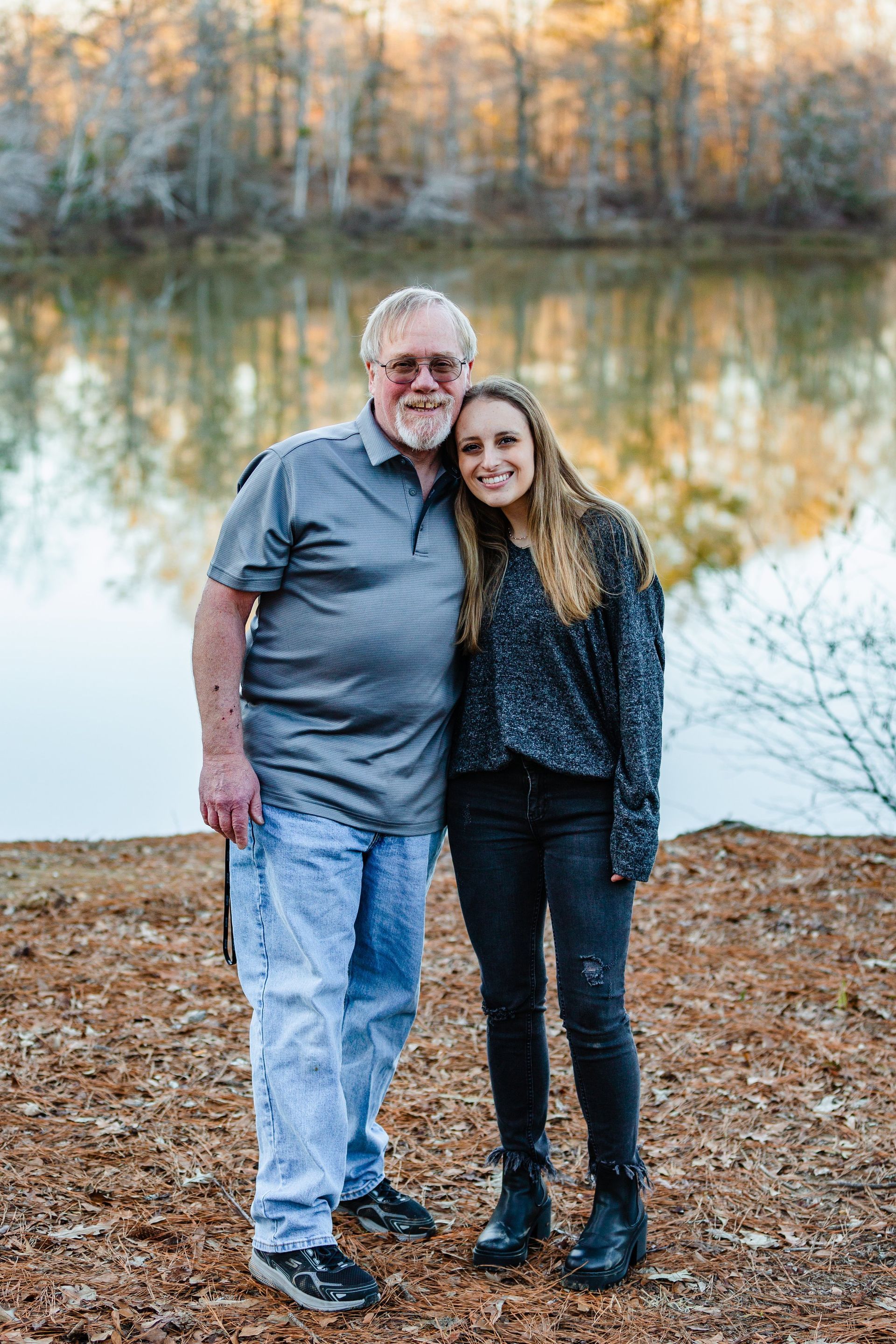 A man and a woman are standing next to each other in front of a lake.
