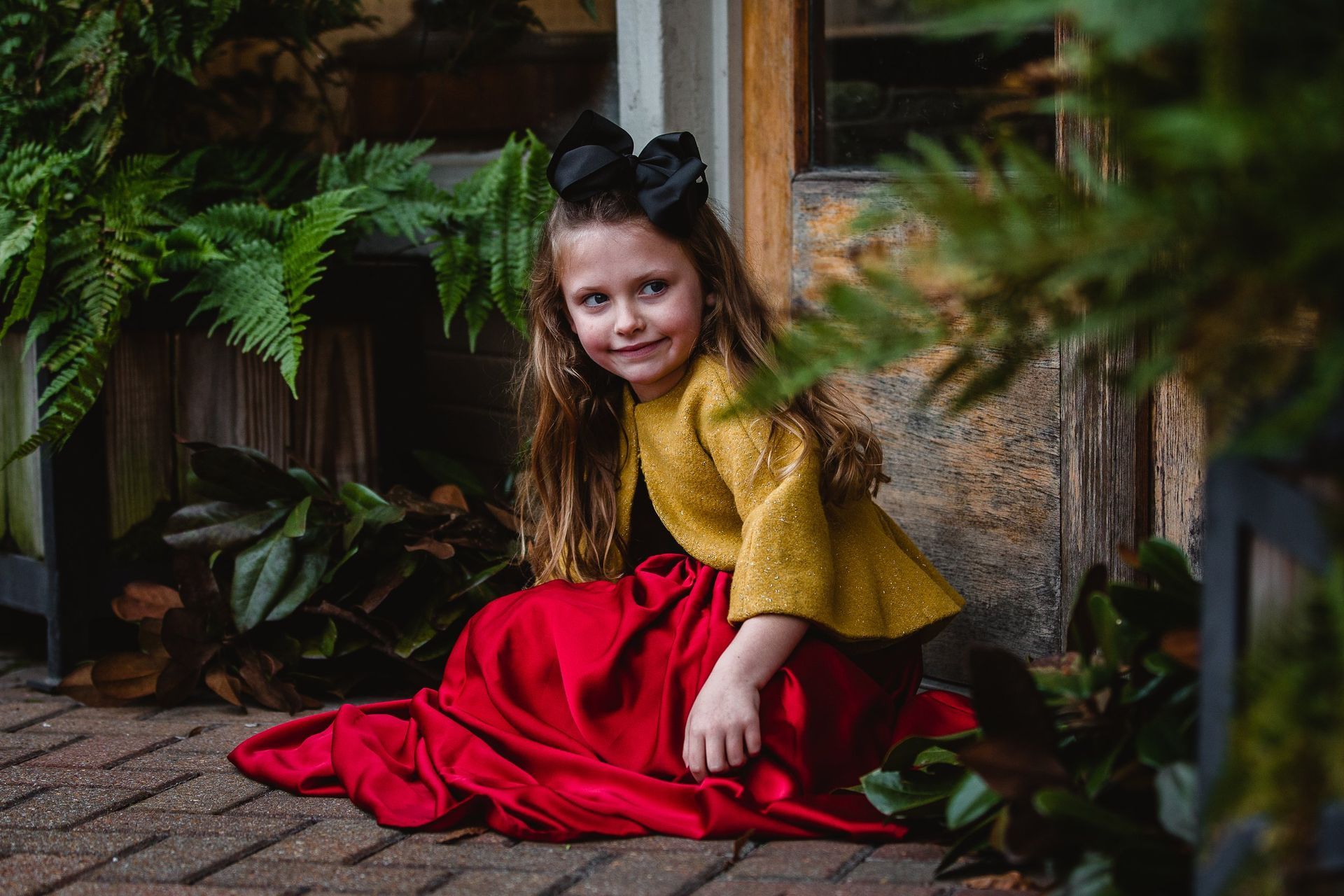 A little girl is sitting on the ground wearing a red skirt and a yellow top.
